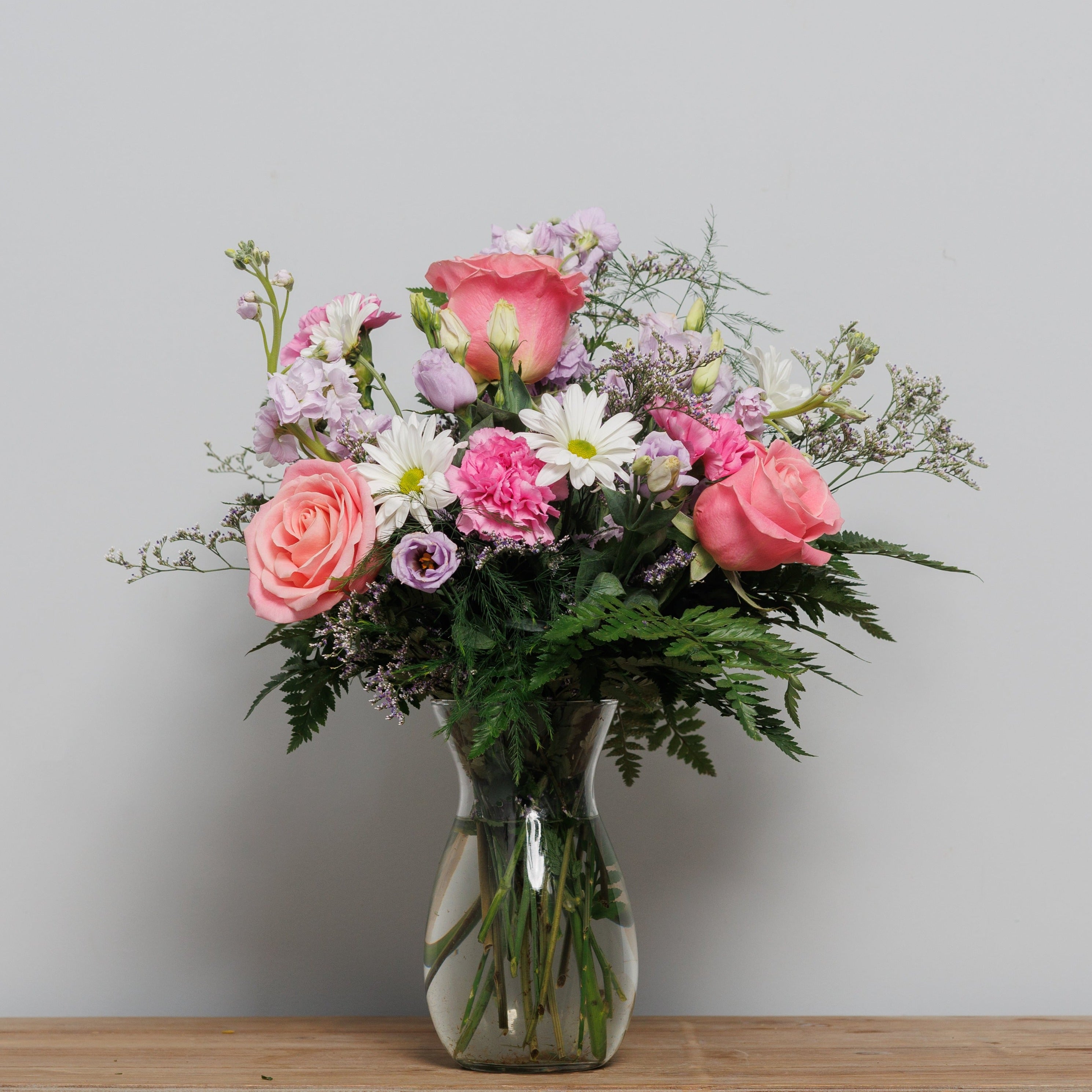 A vase arrangement with pink roses, white daisies and lavender stock