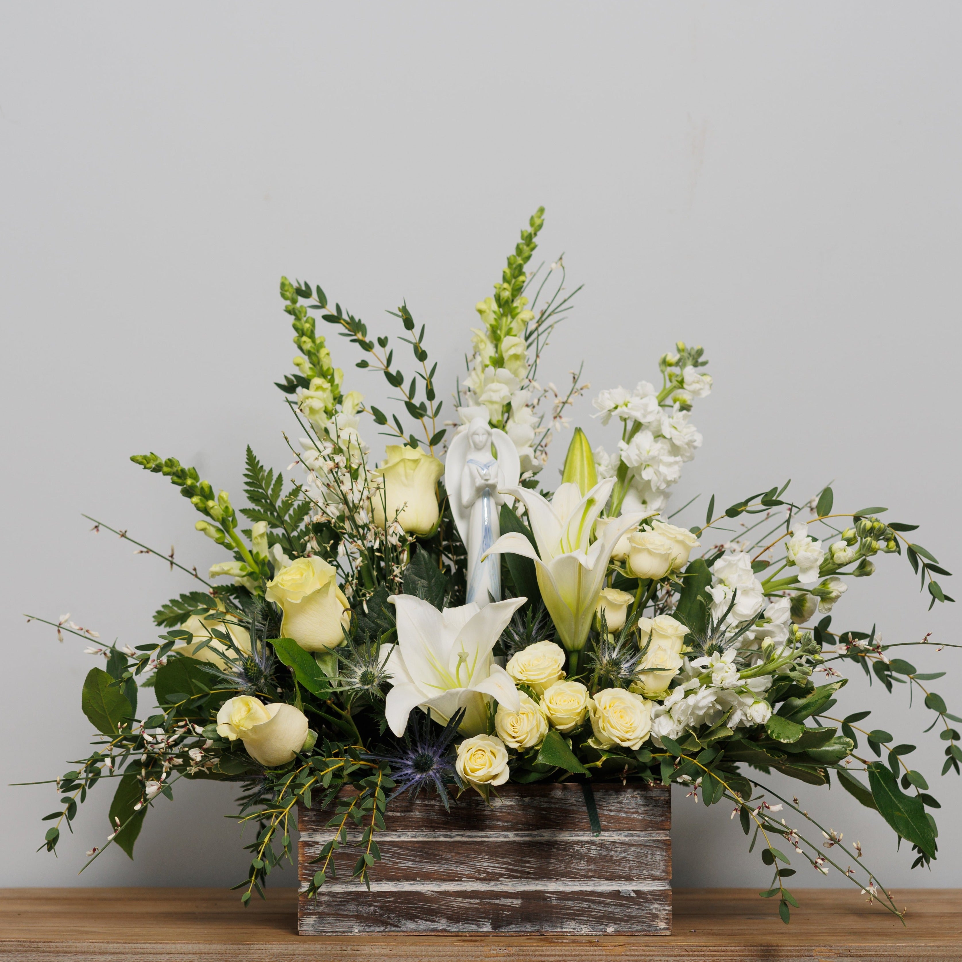 All all white flower arrangement in a distressed box container with a keepsake ceramic angel.