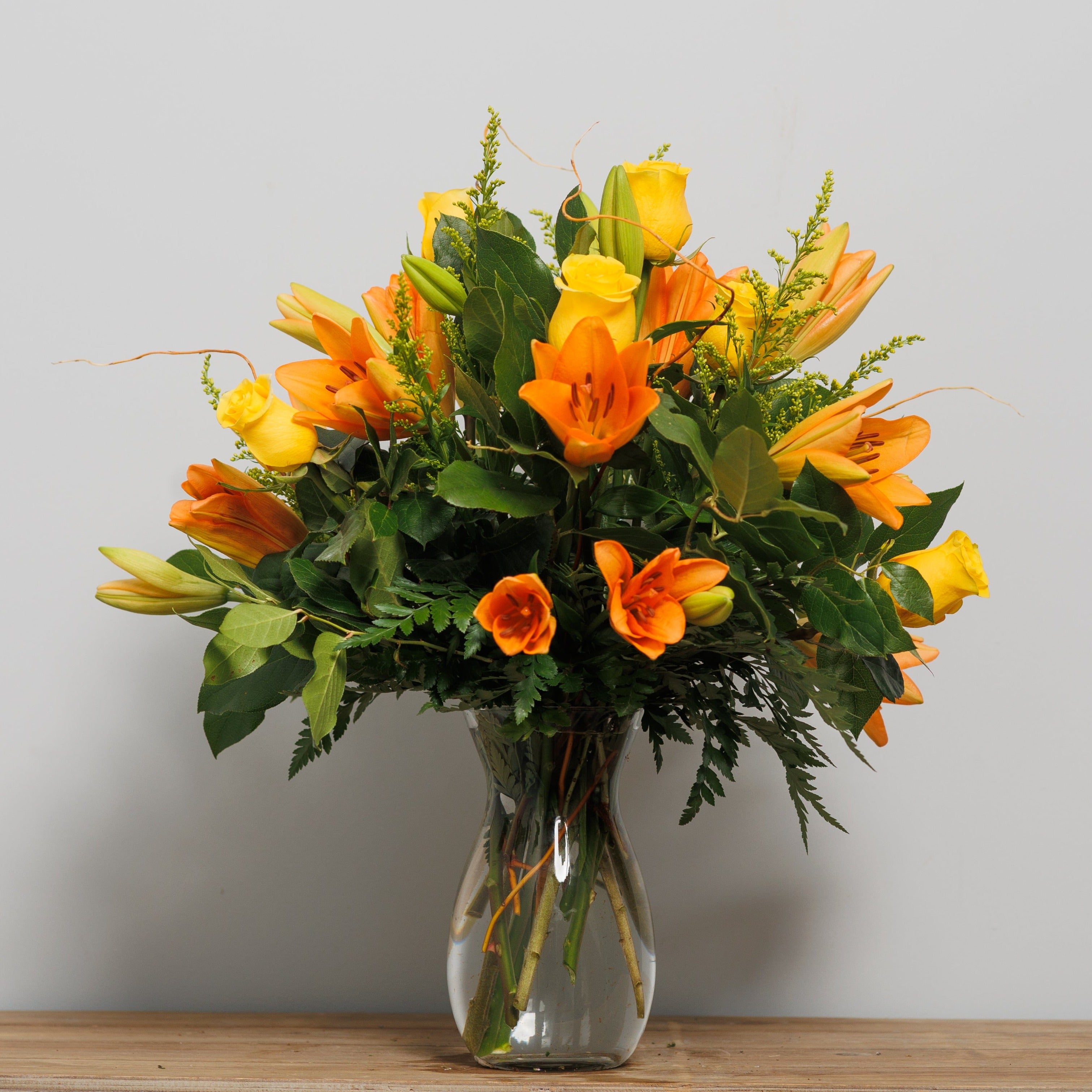 A vase arrangement with orange lilies and yellow roses.