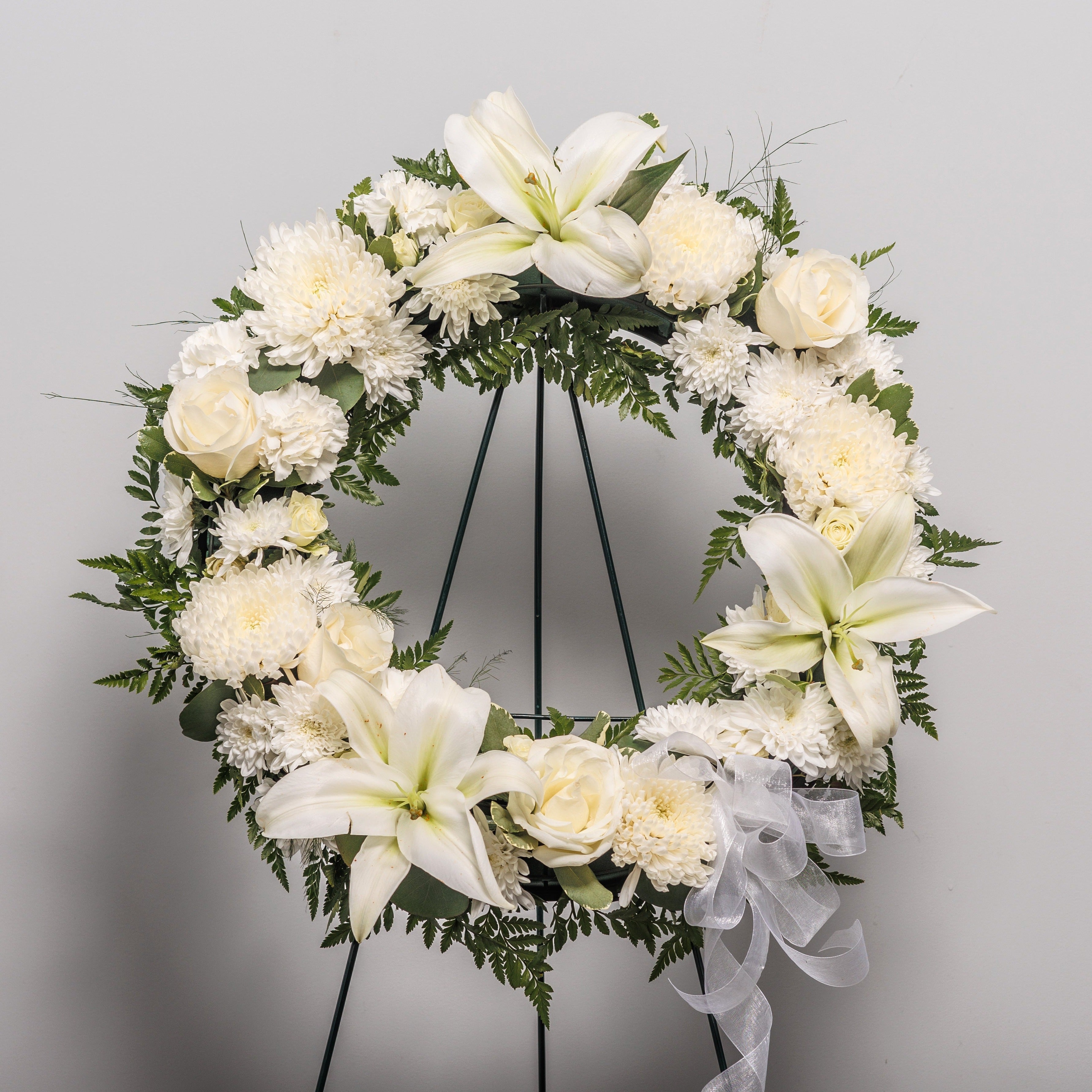 A white wreath on an easel with carnations, roses, mums and lilies.
