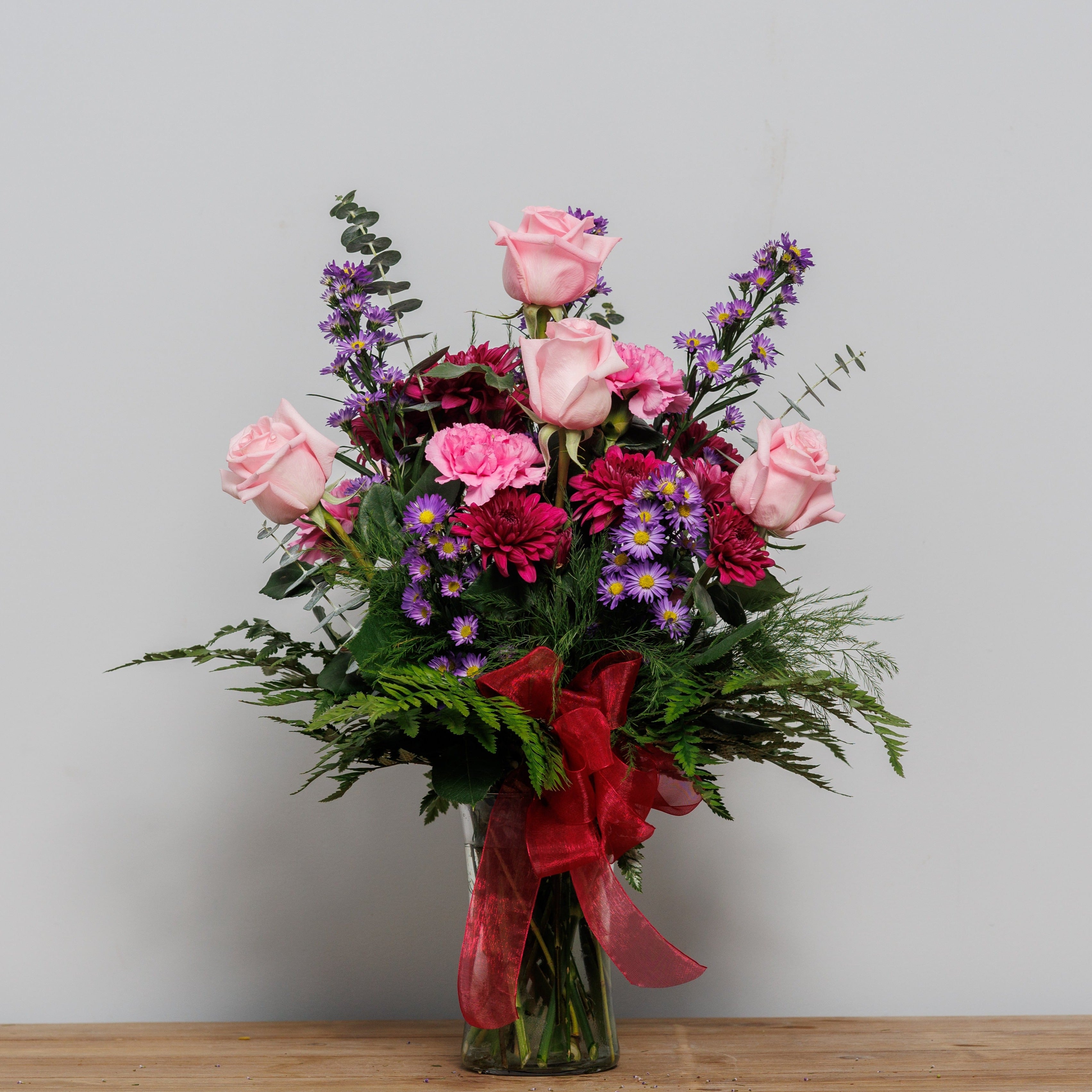 Light pink roses with magenta mums and purple asters arranged in a vase.