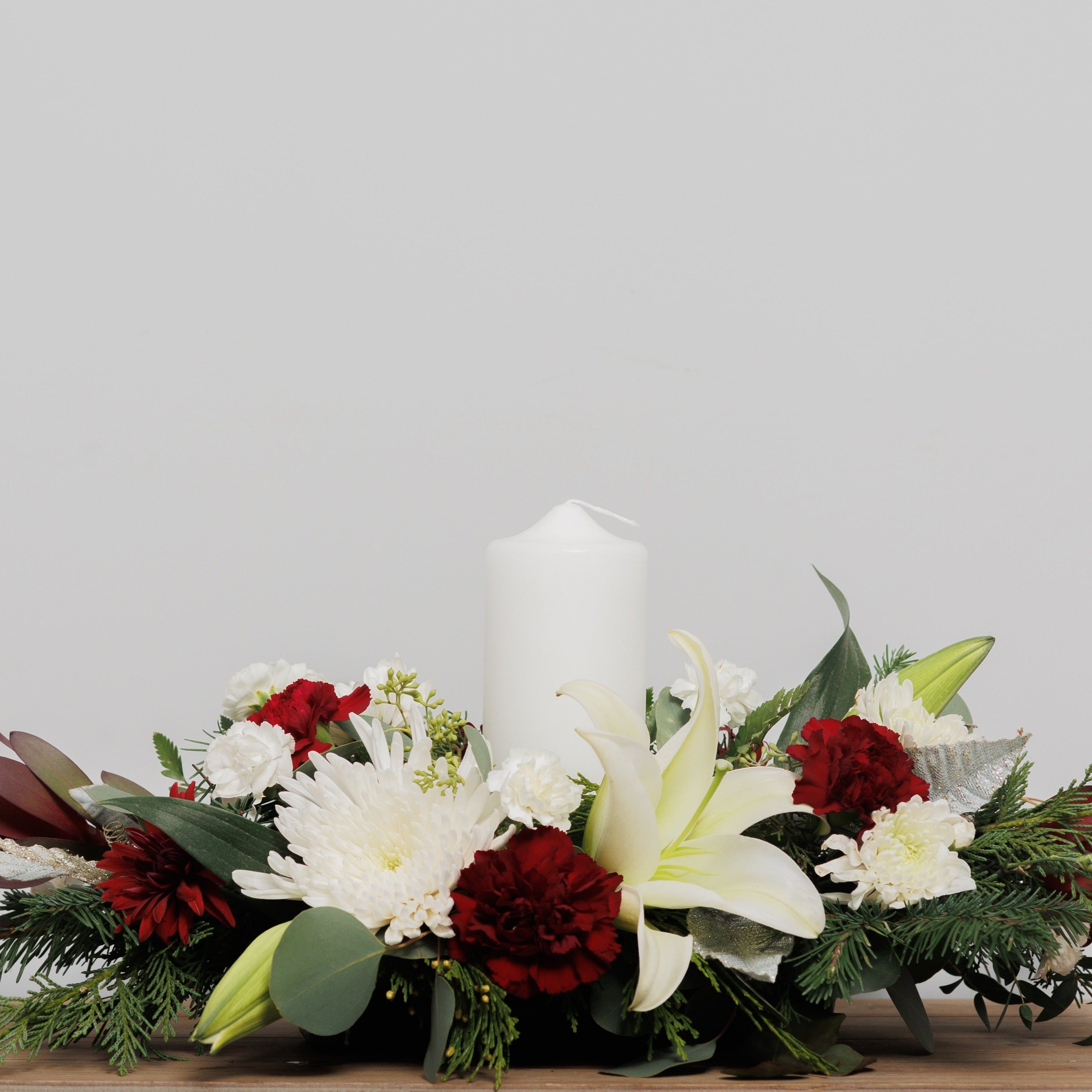 A burgundy and white Christmas centerpiece with a single pillar candle.