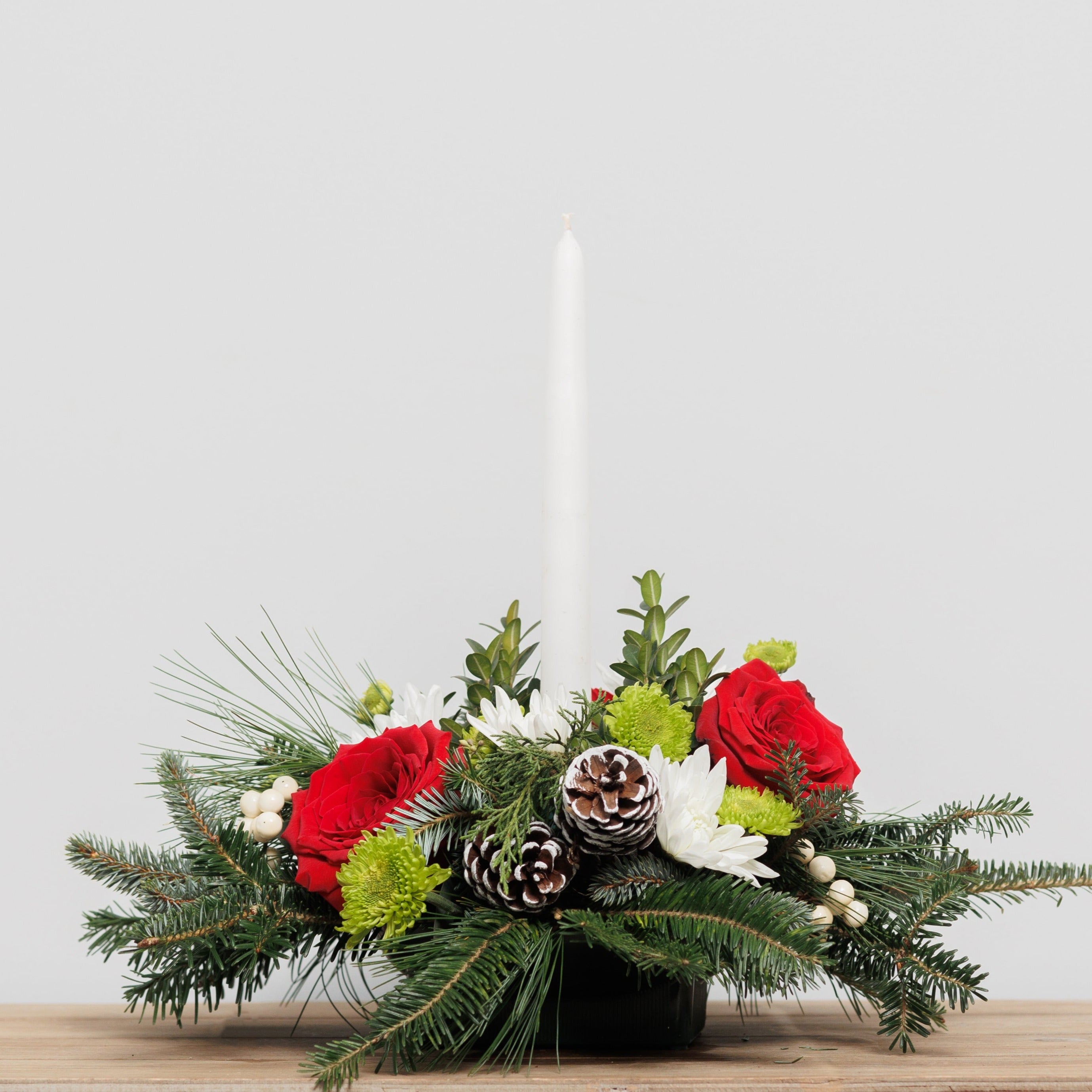 A Christmas centerpiece with red and white flowers, green mums and a white taper candle.