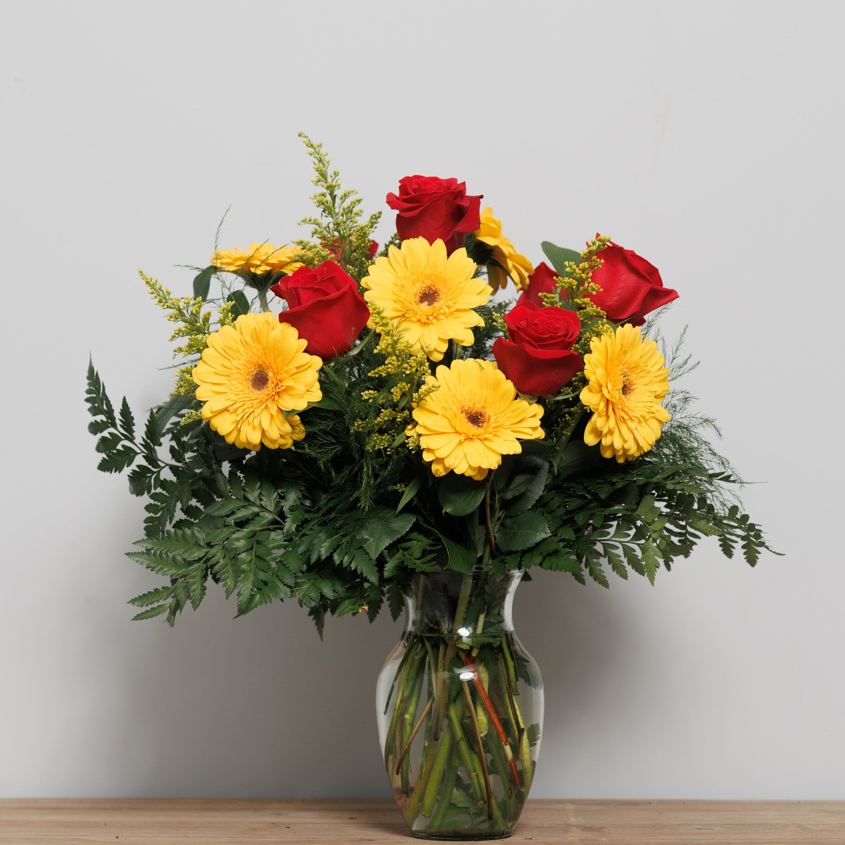 A vase arrangement with red roses and yellow Gerber daisies.