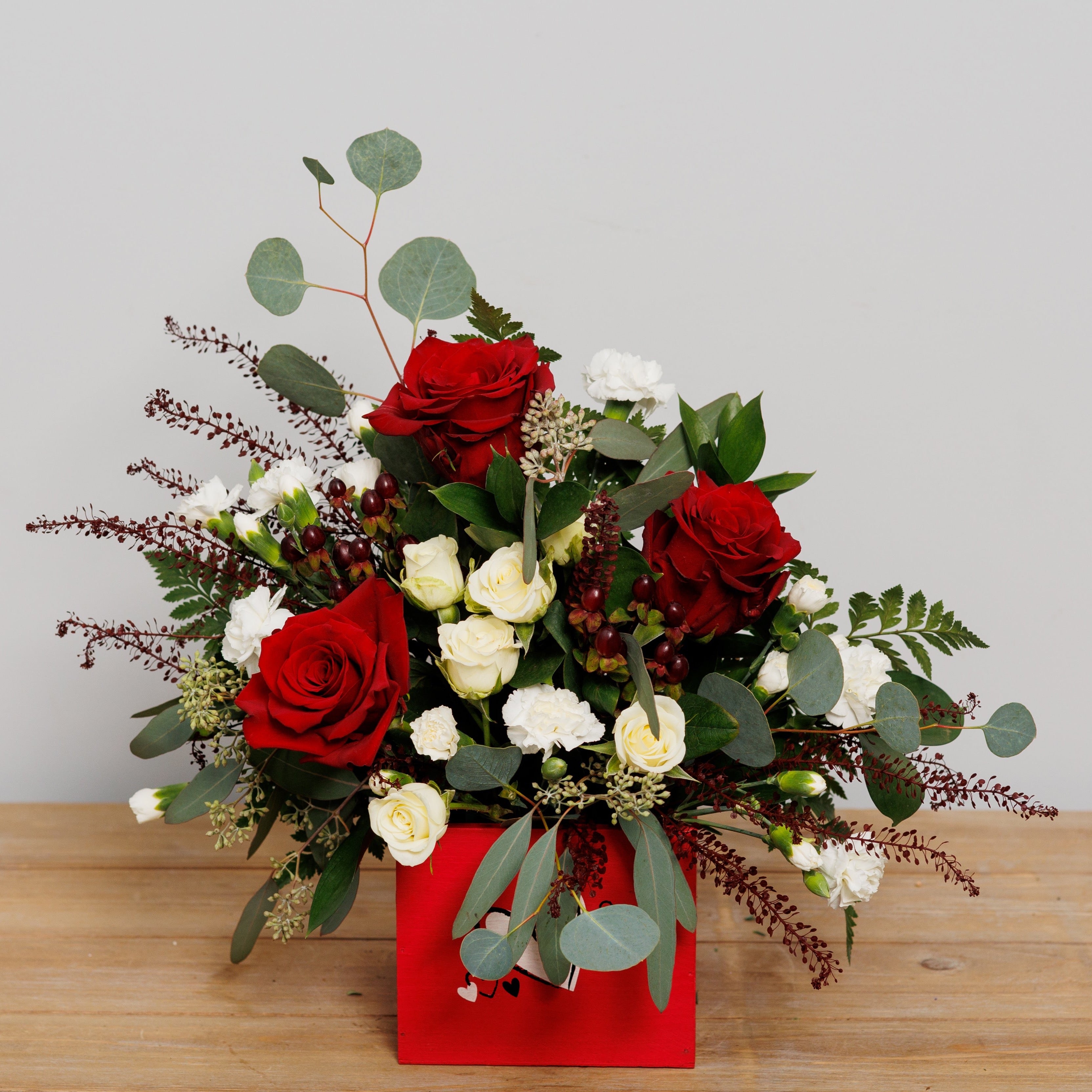 A red keepsake cube with velvet roses, white spray roses and white mini carnations.