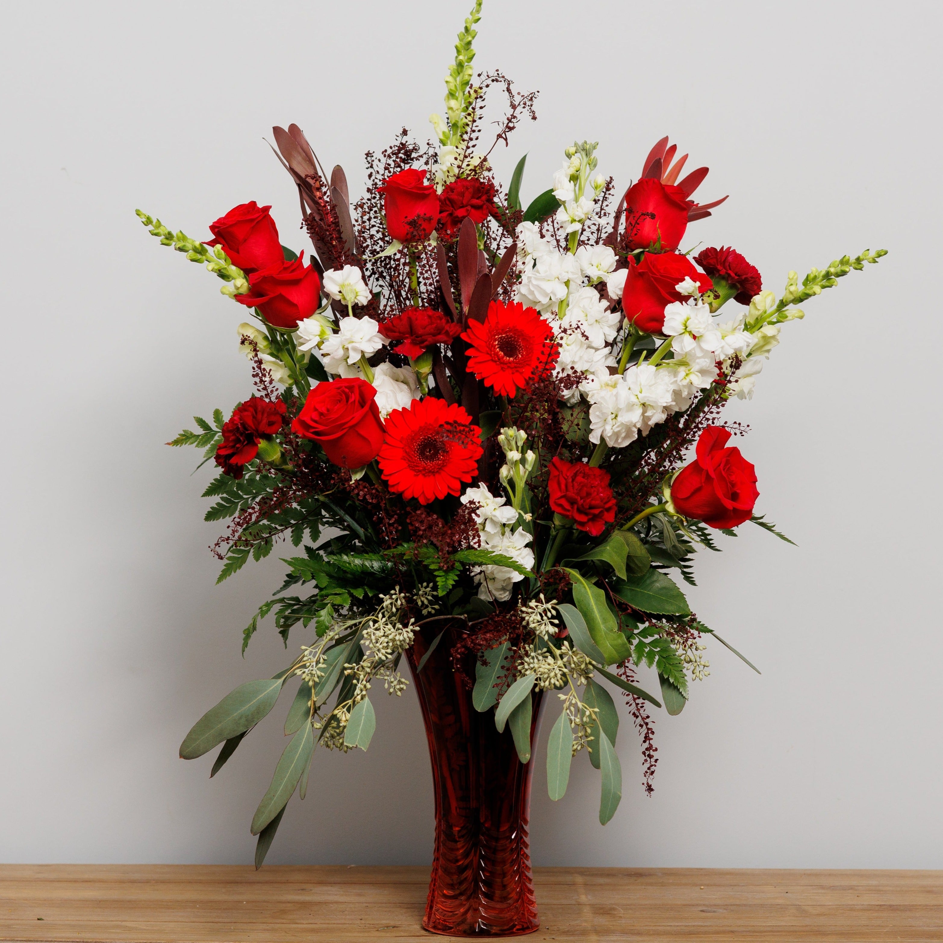 A tall red and white arrangement in a red vase.
