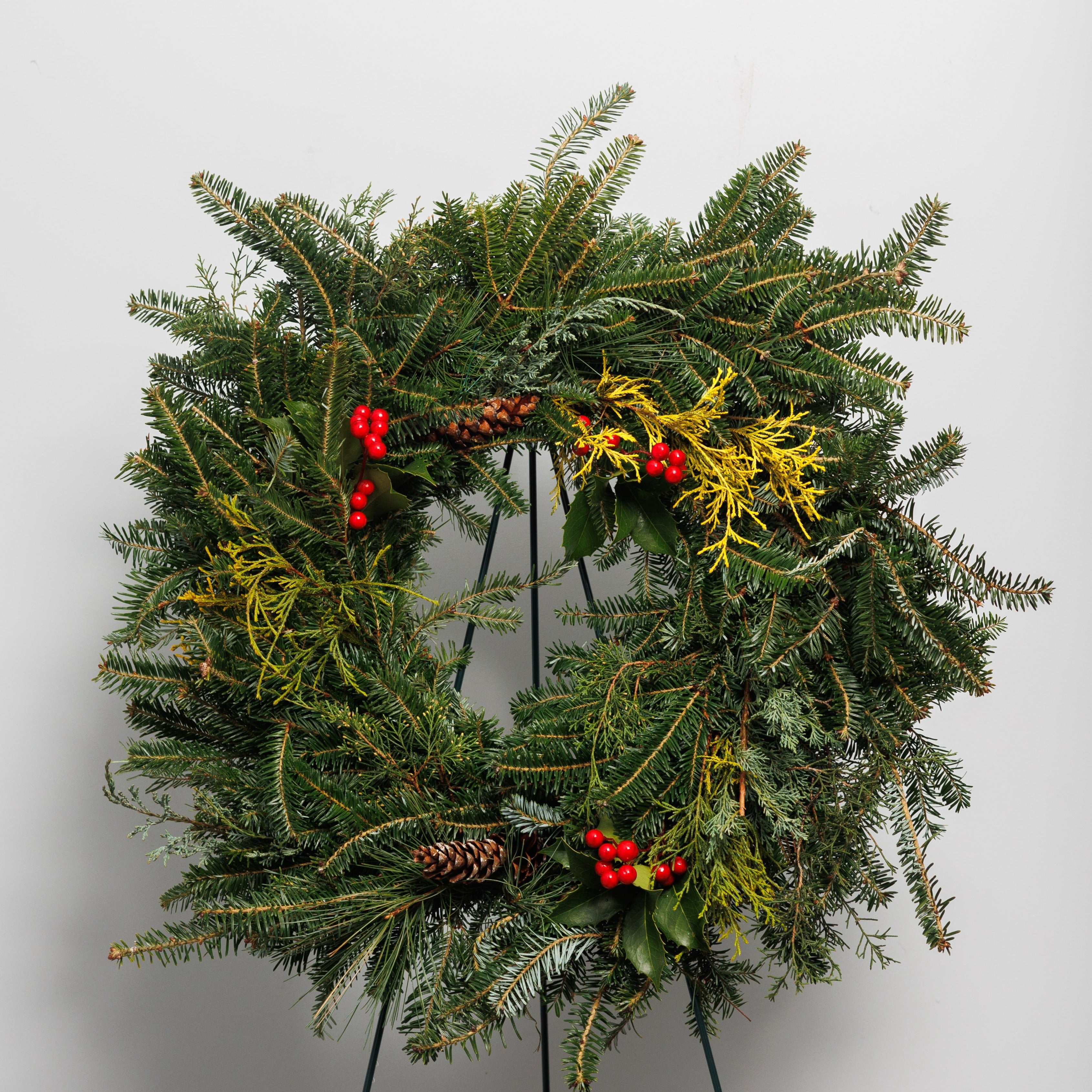 A mixed greens wreath with berries and cones.