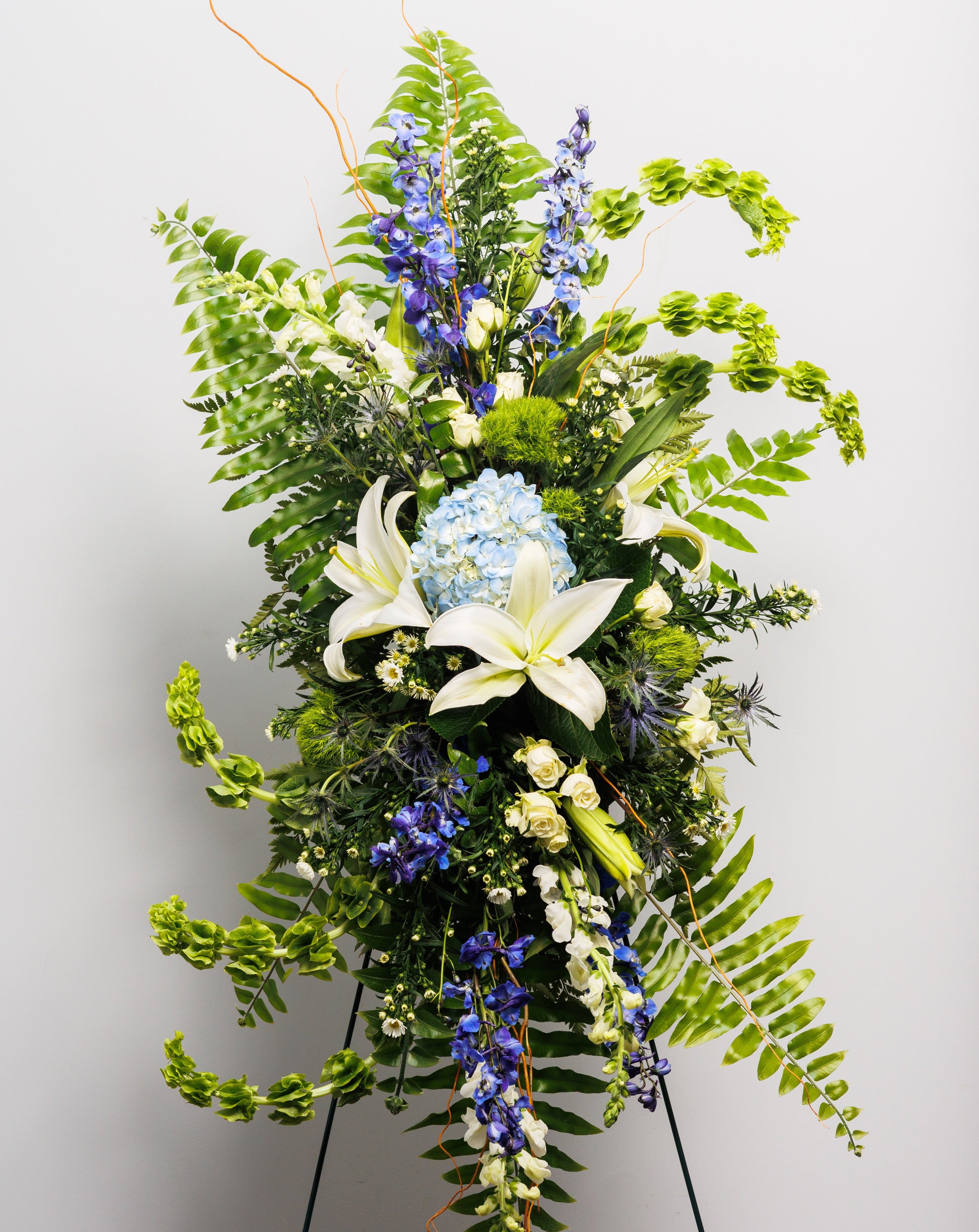 A standing spray with white lilies, blue hydrangea, bells of Ireland and blue delphinium.