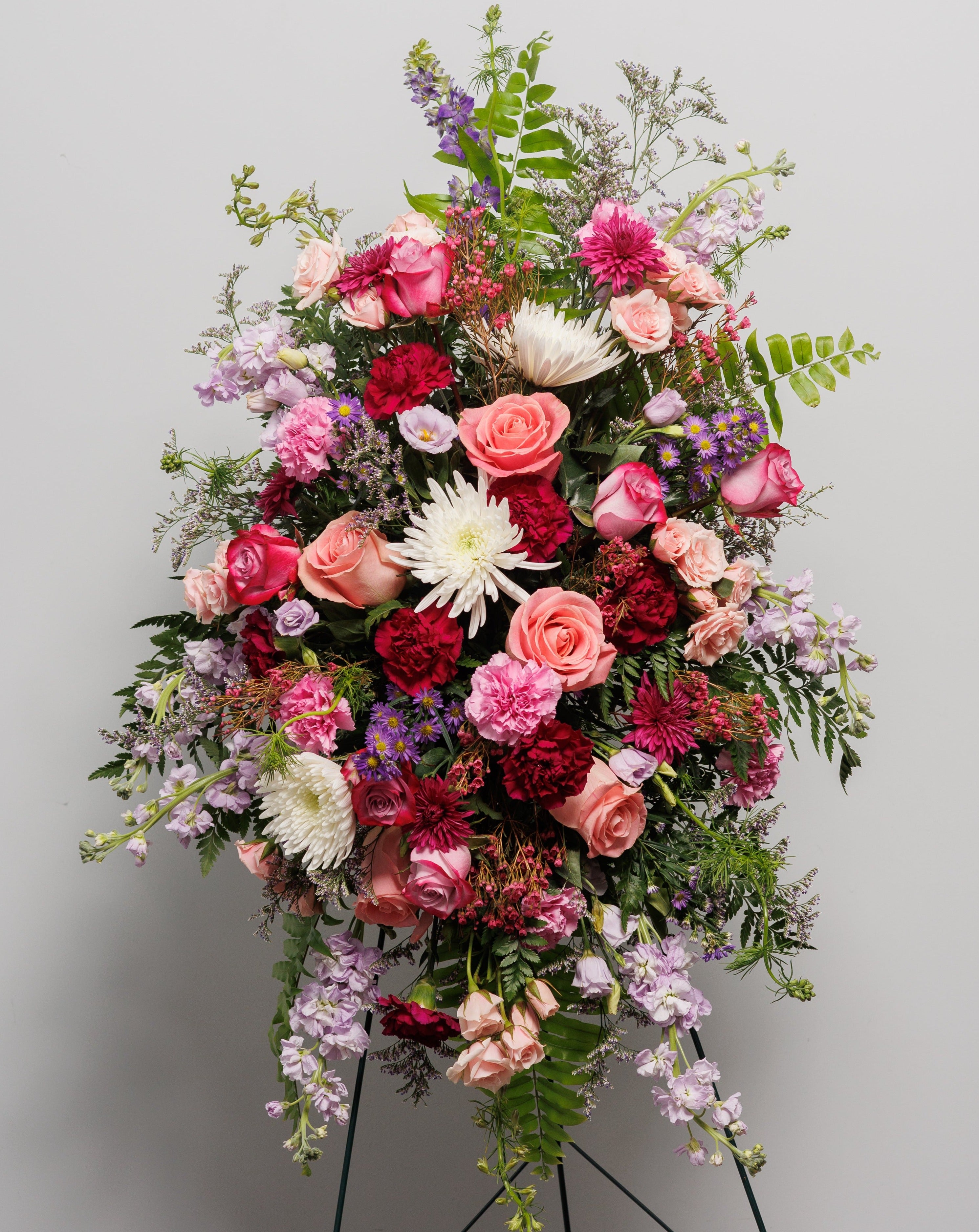 A standing spray primarily in shades of purple including roses, sock and carnations.