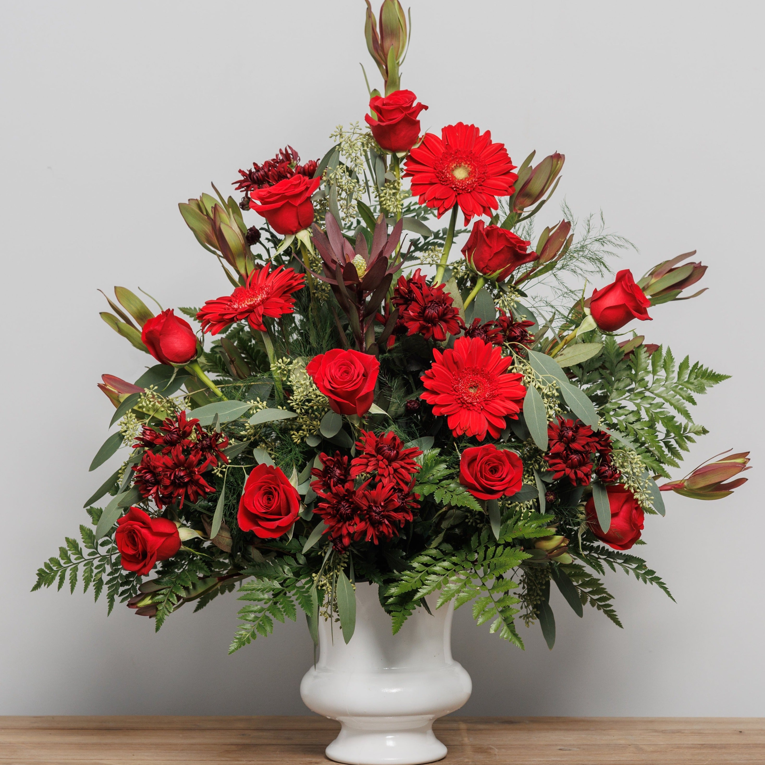 An urn arrangement with red roses and safari sunset.