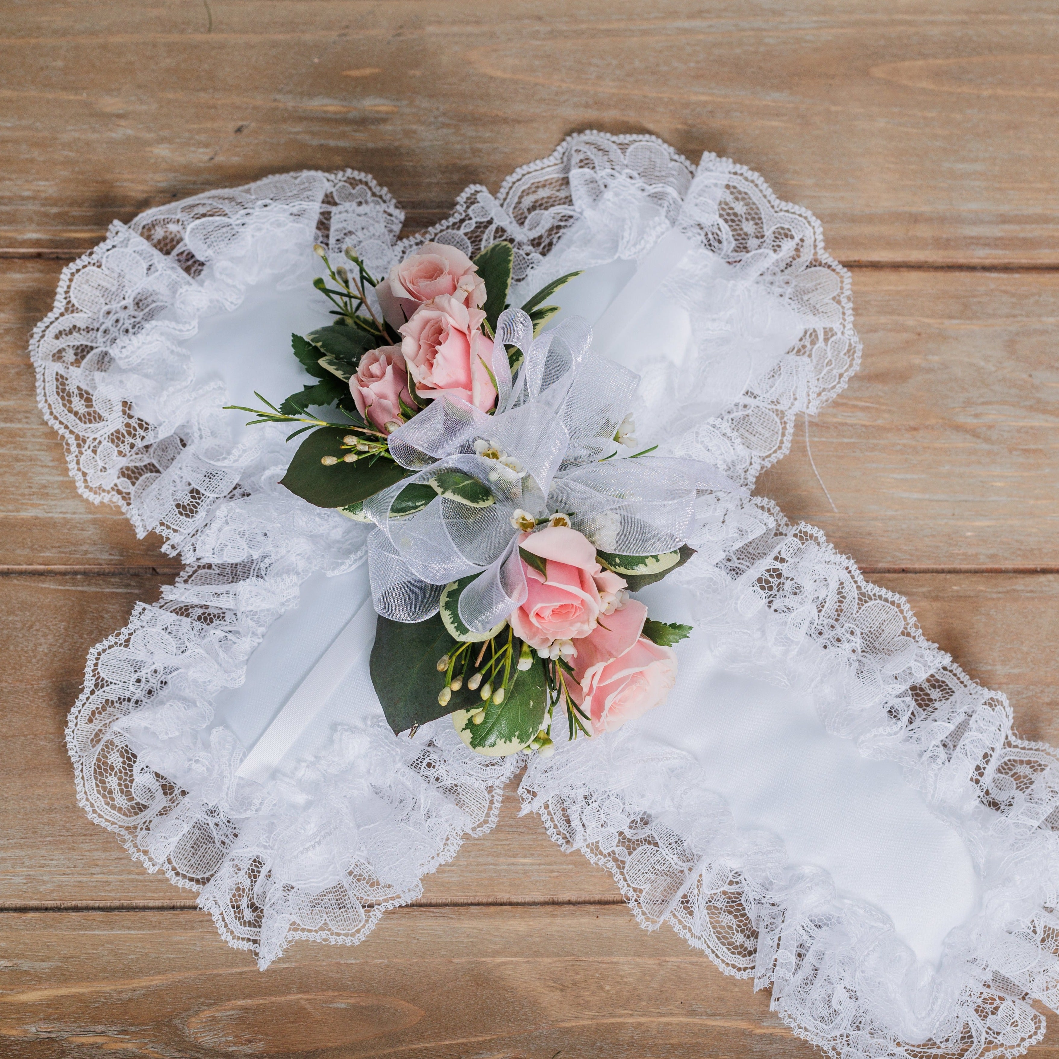 A white satin pillow with light pink spray roses and white sheer ribbon.
