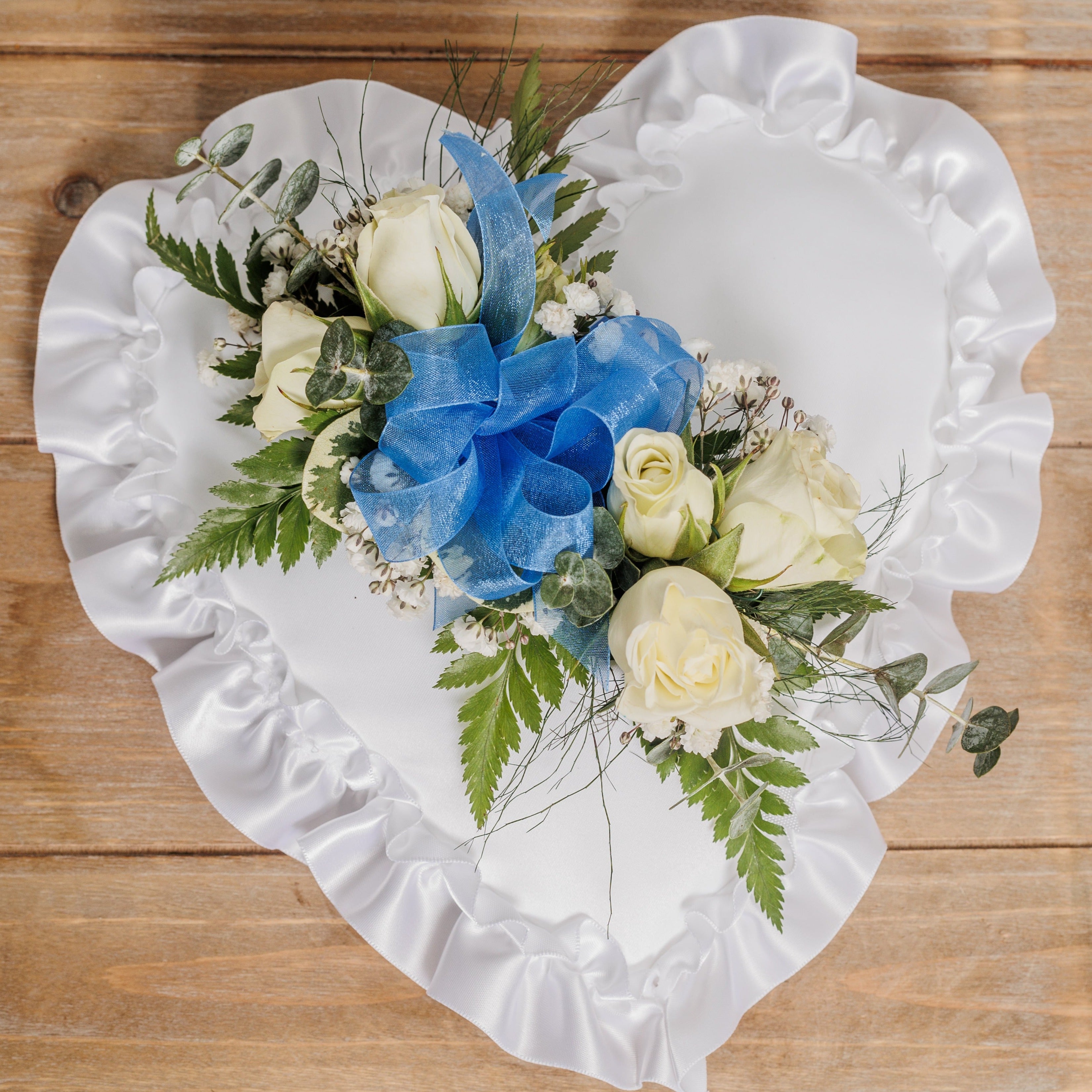 A white satin heart pillow with white roses and blue ribbon.