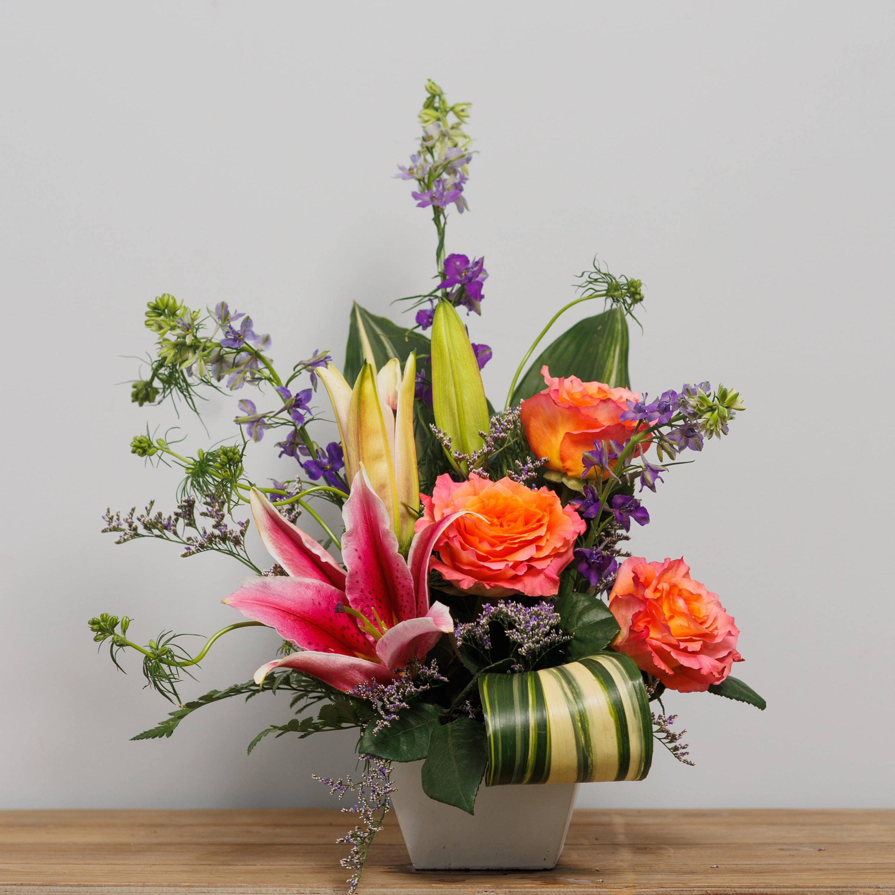 A tropical arrangement with orange roses and stargazer lilies.