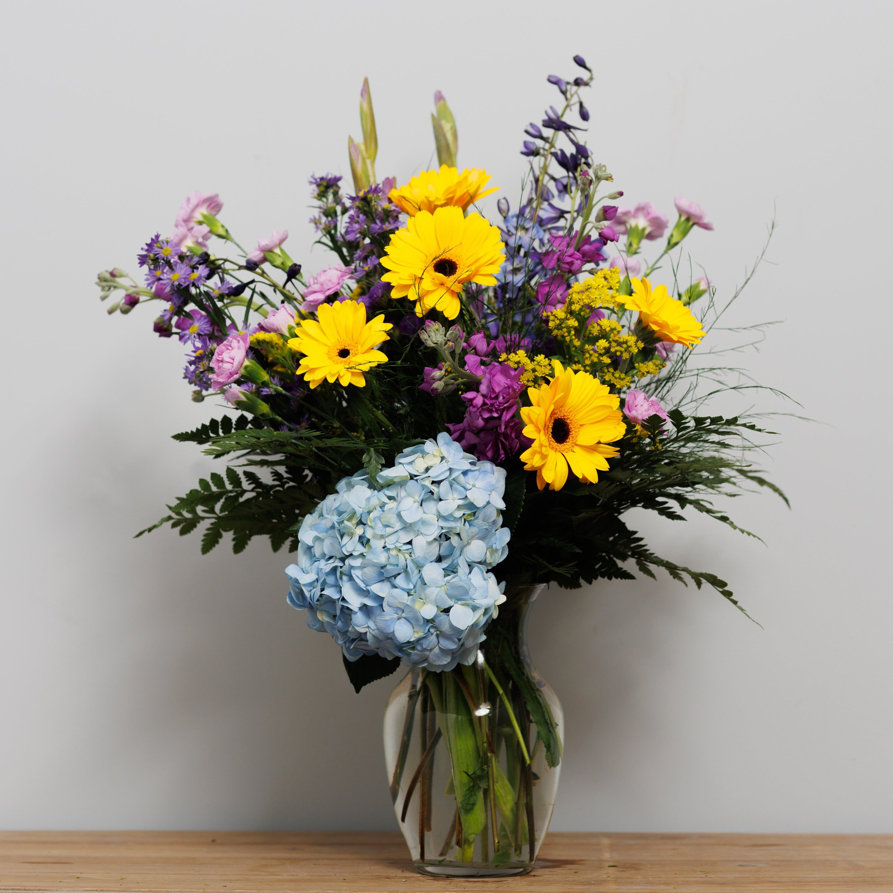 Yellow Gerber daisies with blue and purple blooms in a vase.