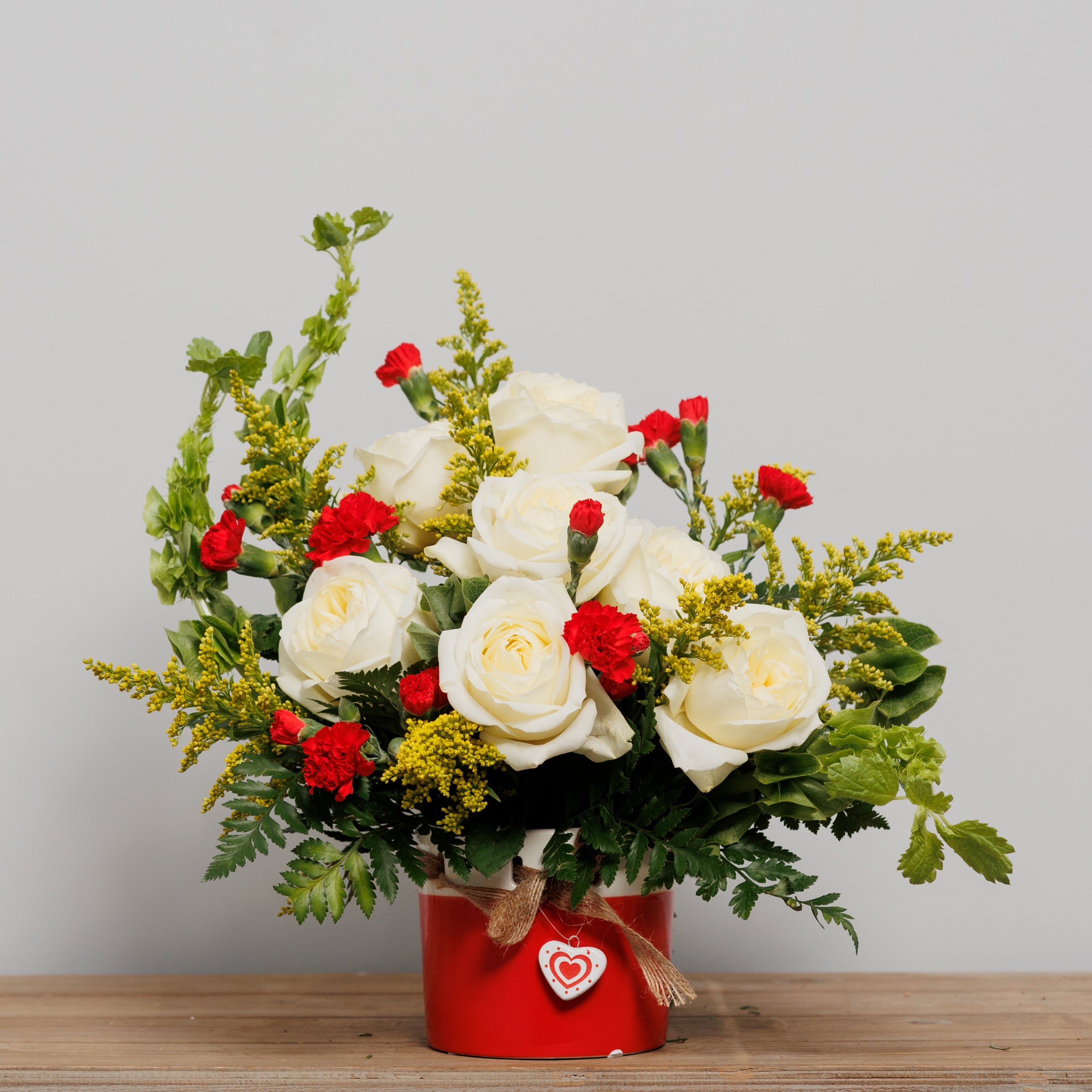 A flower arrangement with white roses and bells of Ireland in a keepsake heart cylinder.