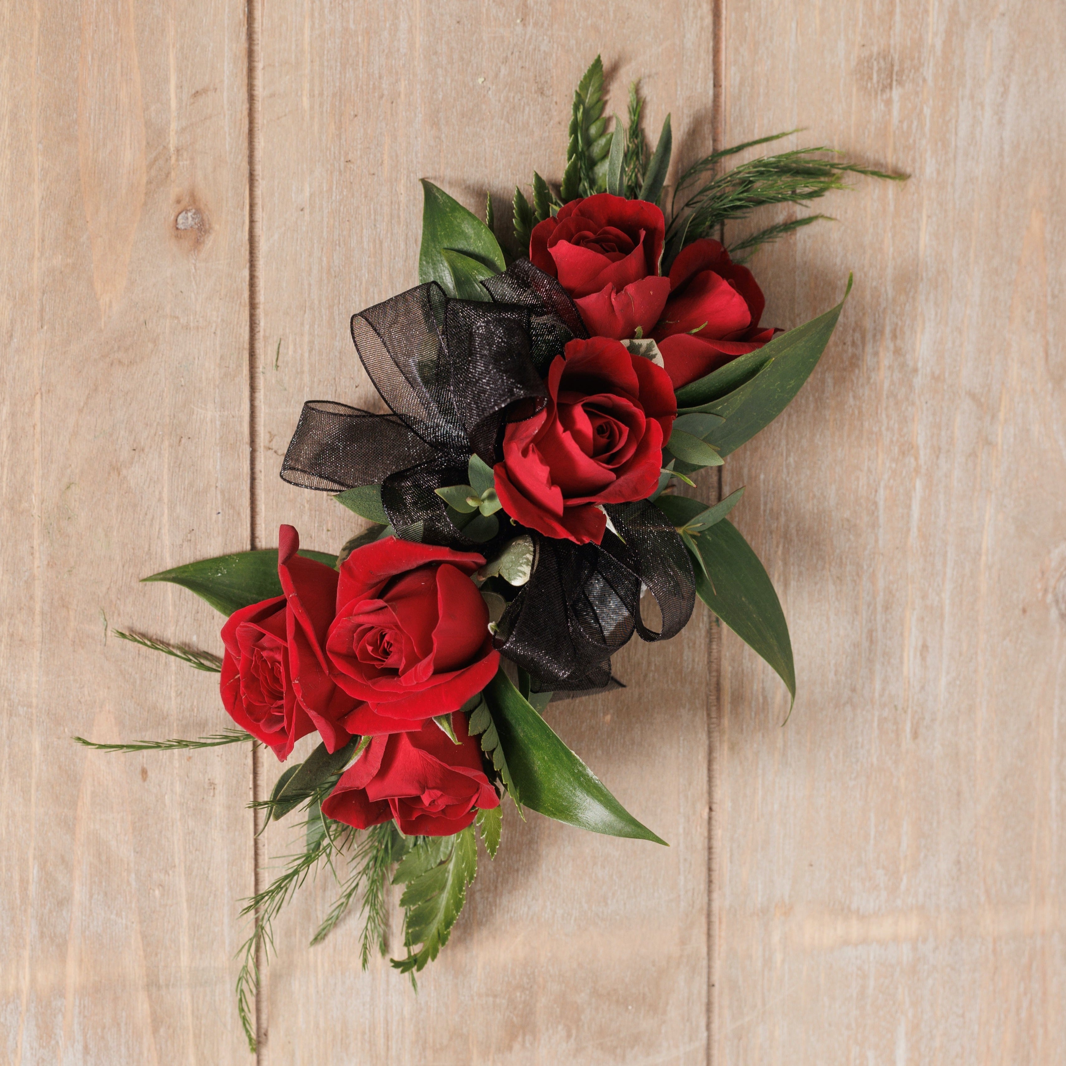A wrist corsage with red spray roses and black ribbon.