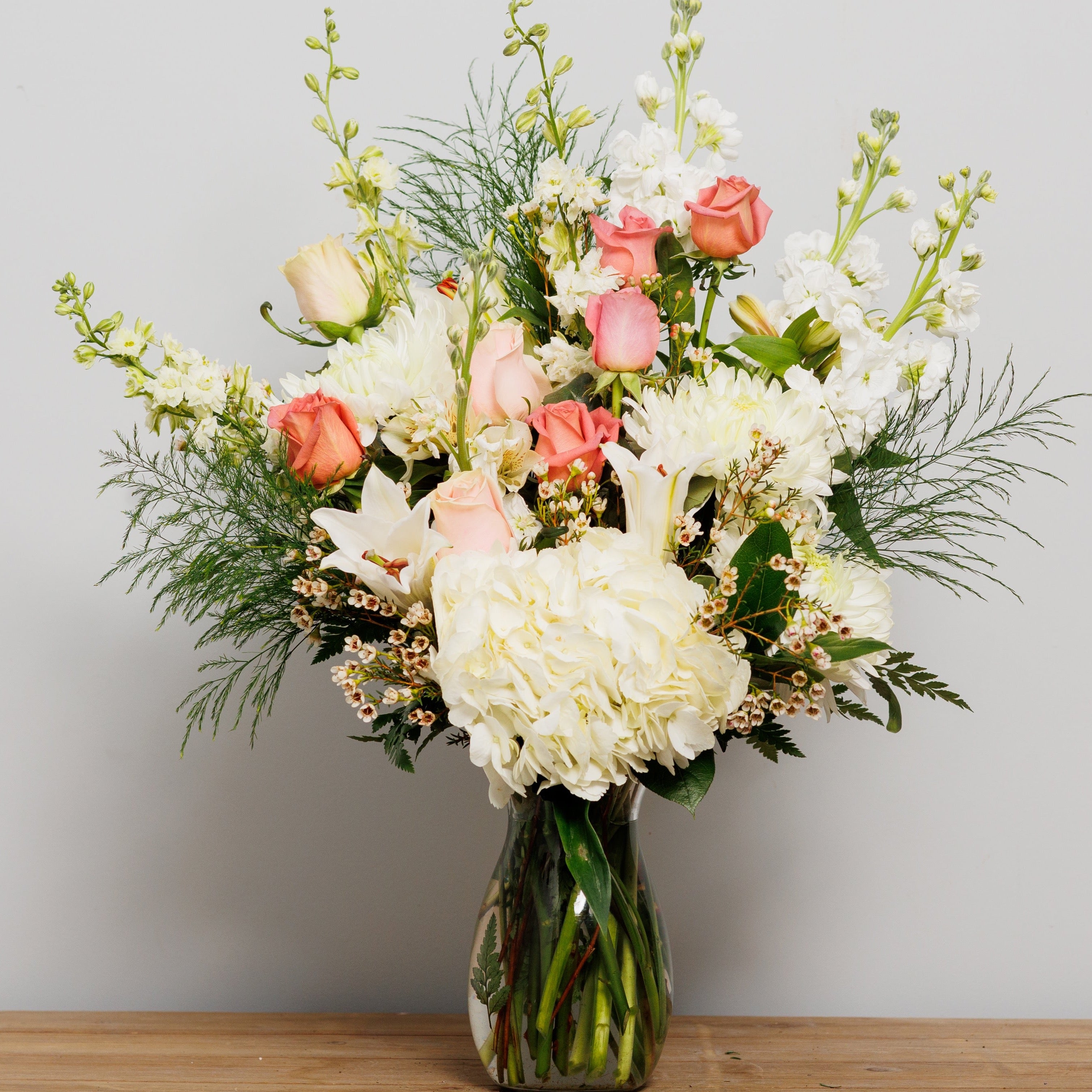 A vase arrangement with a white hydrangea, mauve roses and other white flowers.