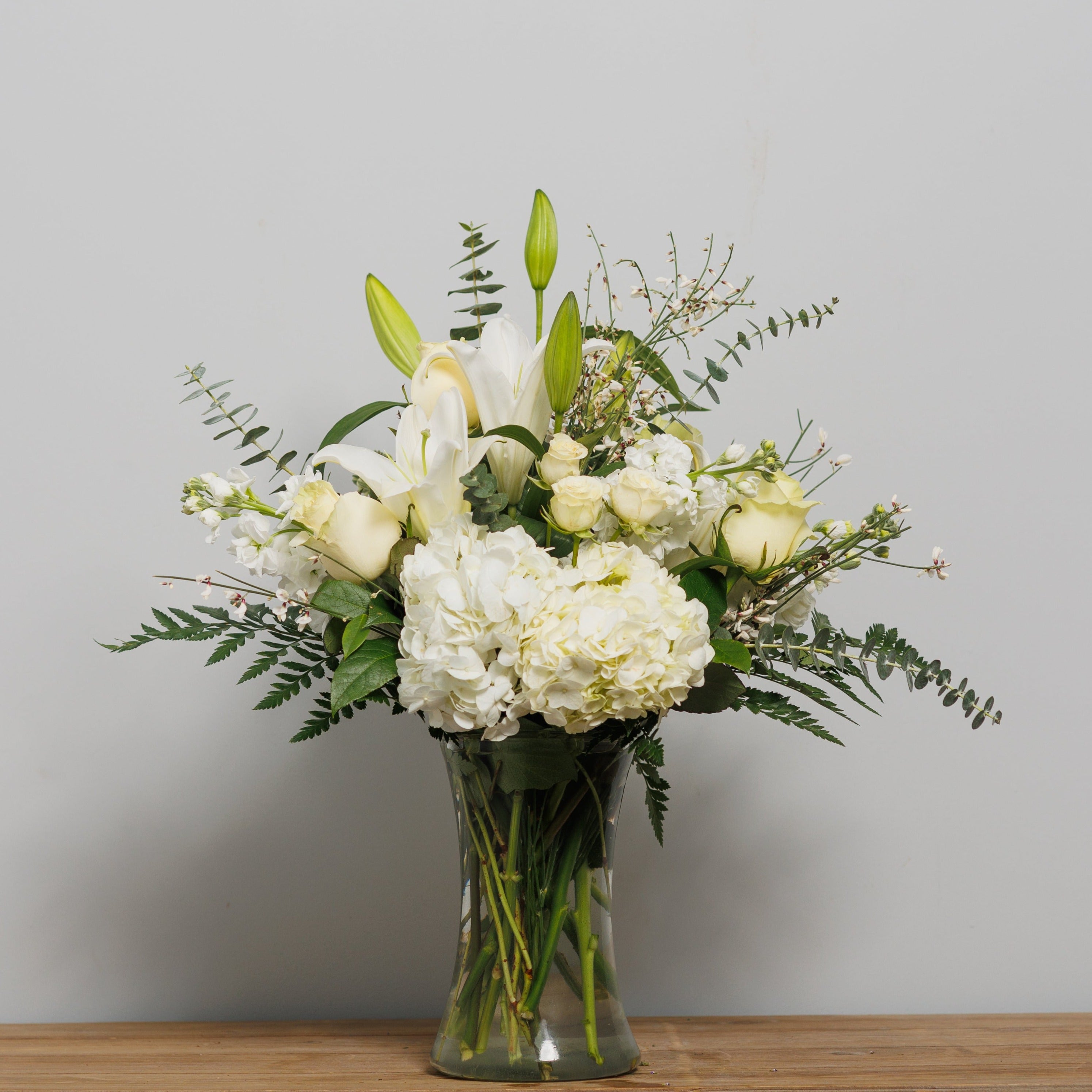 An all white flower arrangement with roses, lilies and hydrangea.