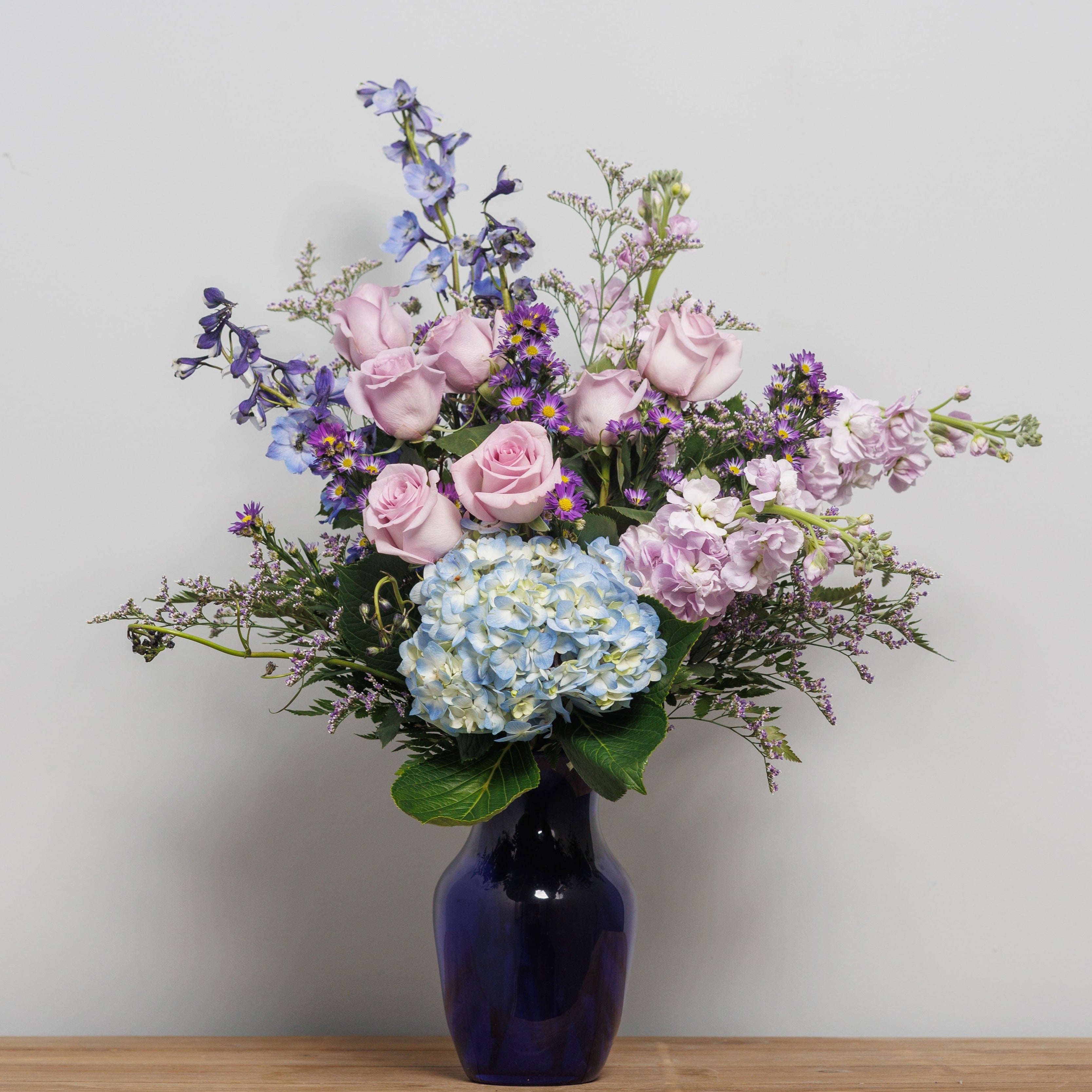 A flower arrangement with blue and purple flowers in a blue vase.