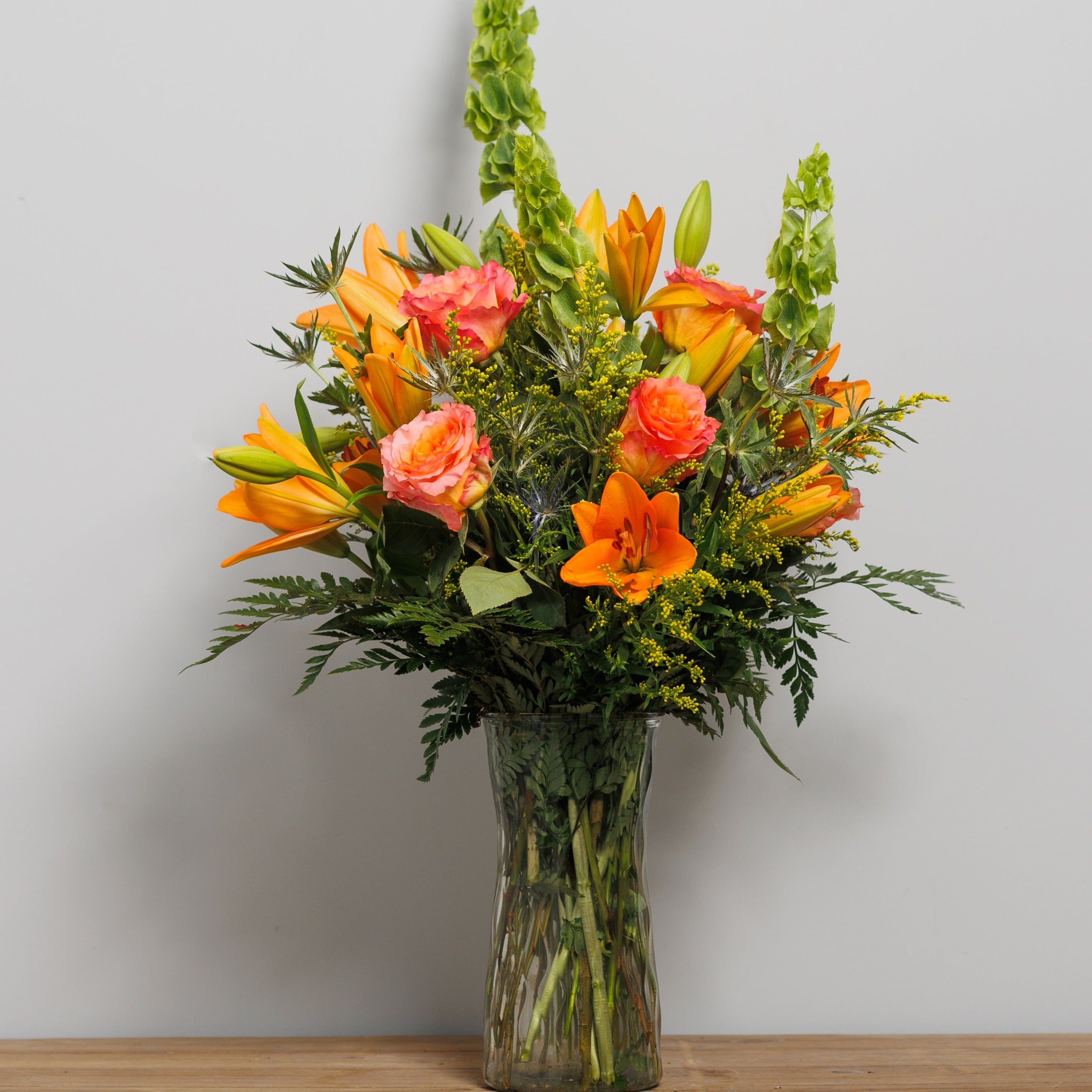 Orange lilies, free spirit roses and Bells of Ireland in a vase arrangement.