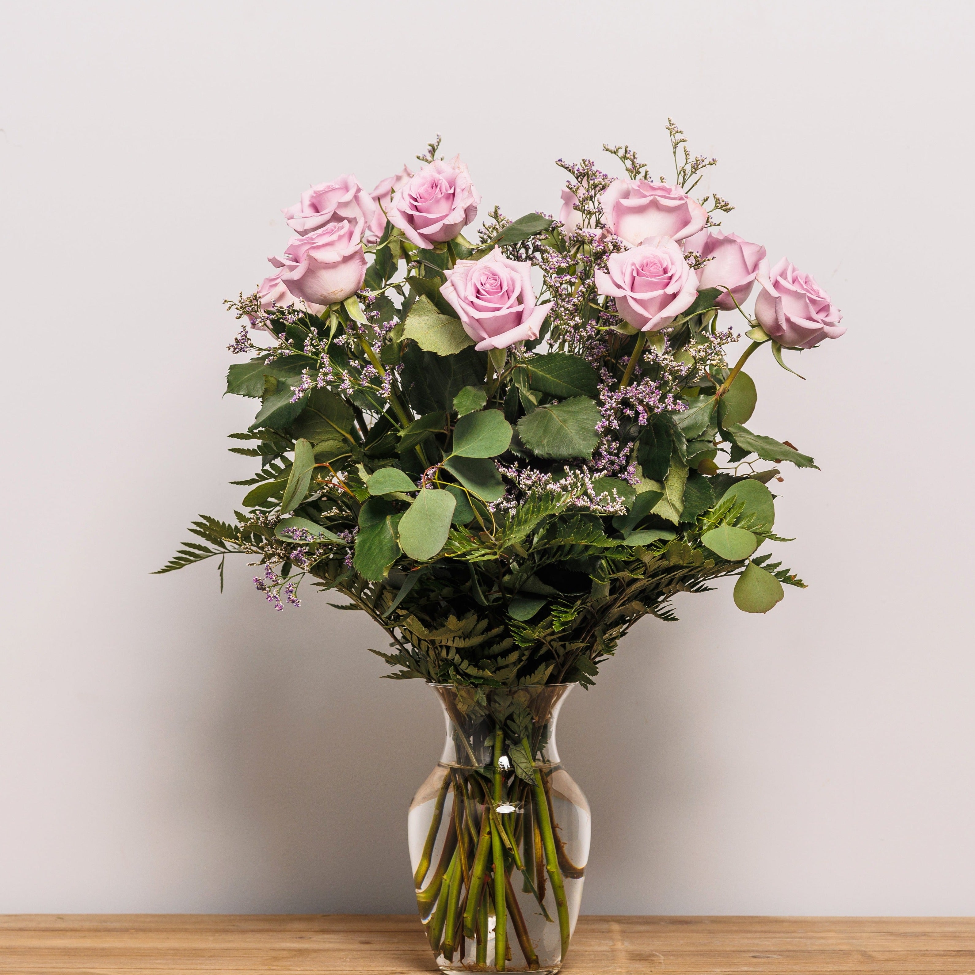 A dozen lavender roses arranged in a vase.