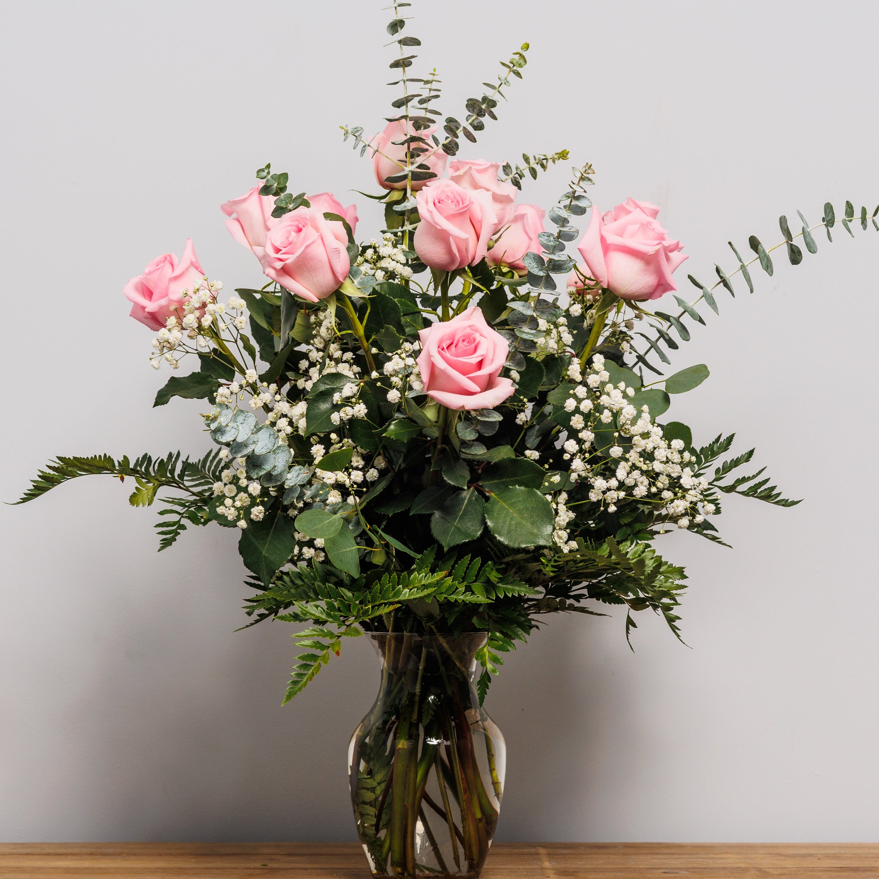 A dozen light pink roses arranged in a vase.