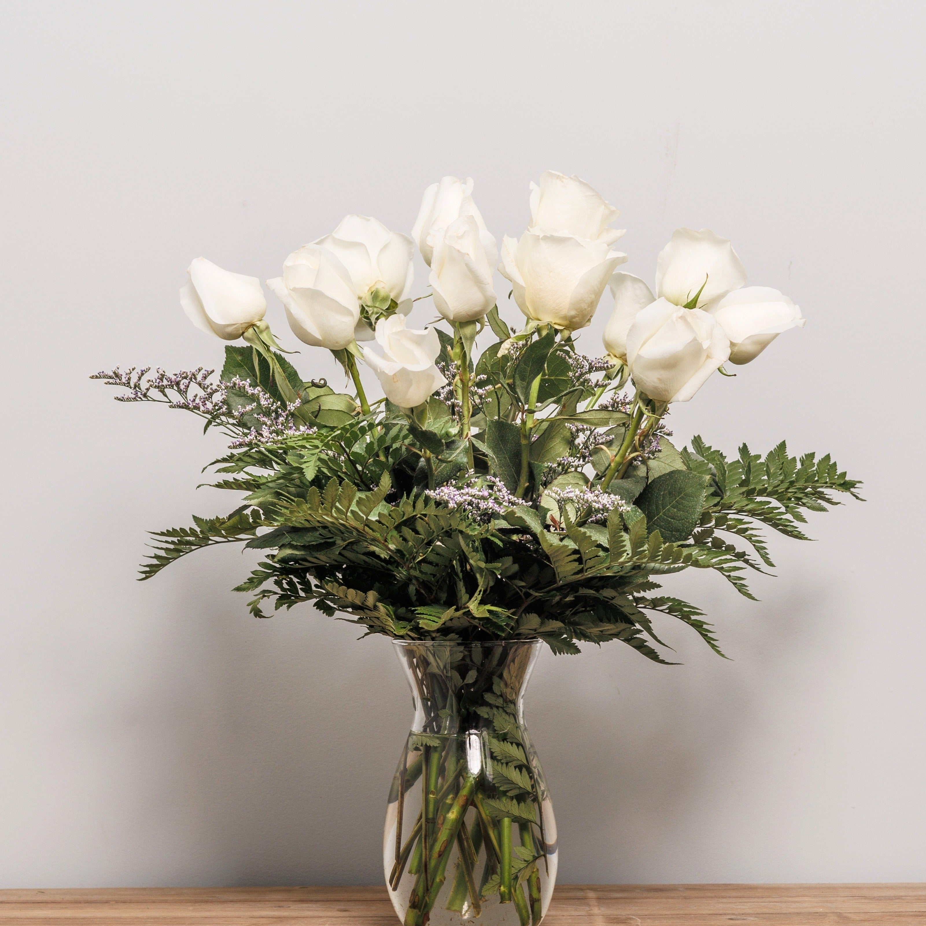 A dozen white roses arranged in a vase.