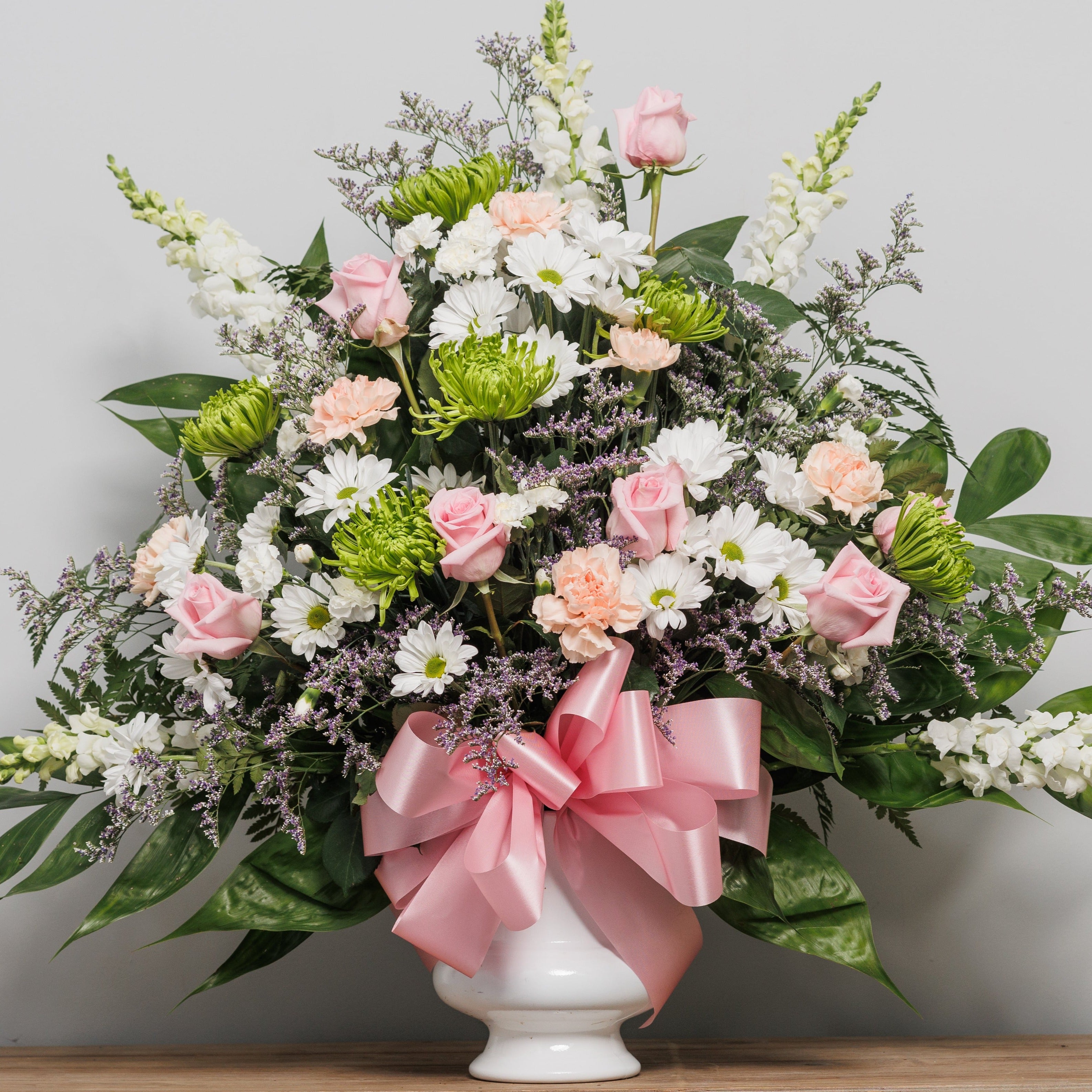 An urn arrangement with white daisies, pink roses and green mums.