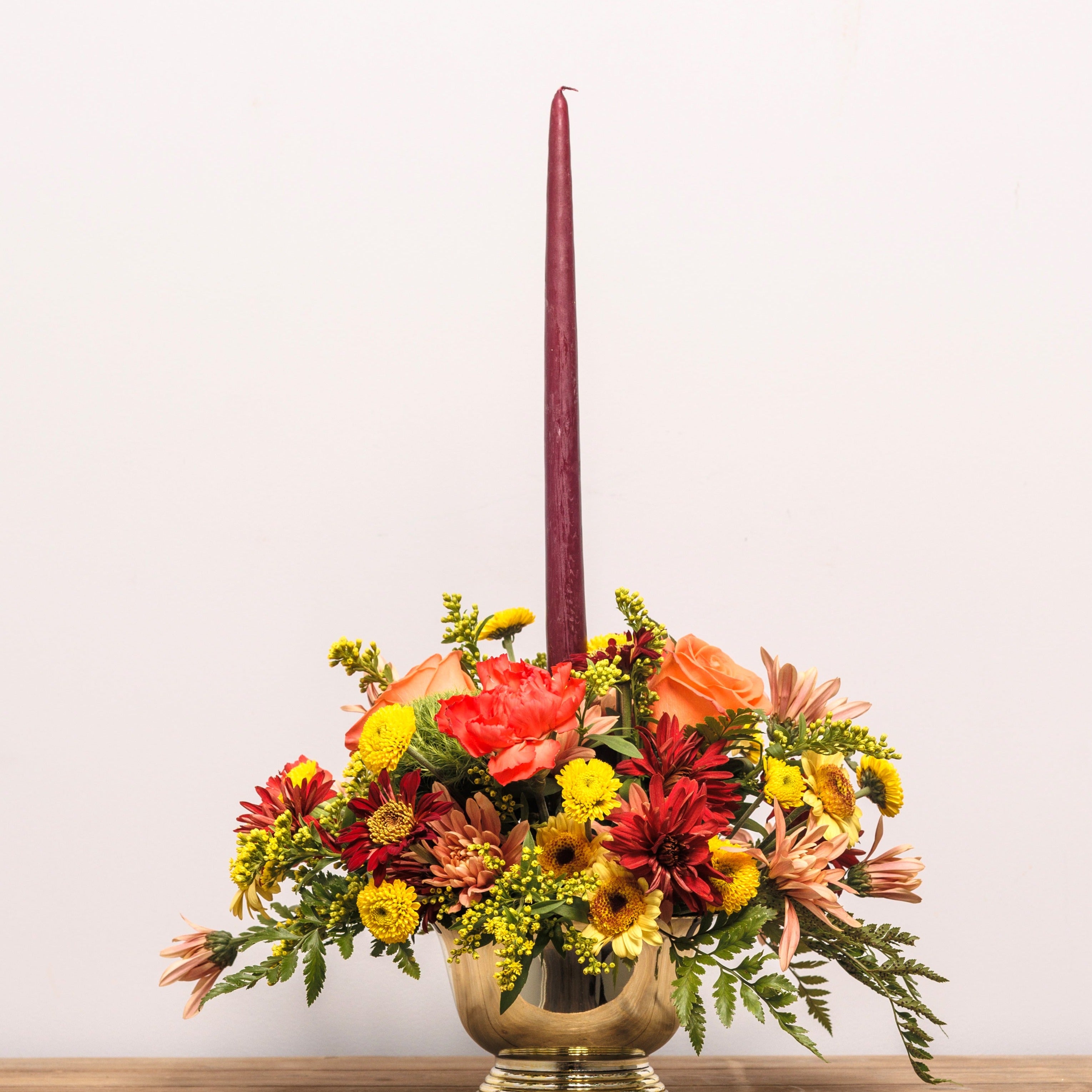 A small fall centerpiece with autumn colors, a taper candle and a golden vase.