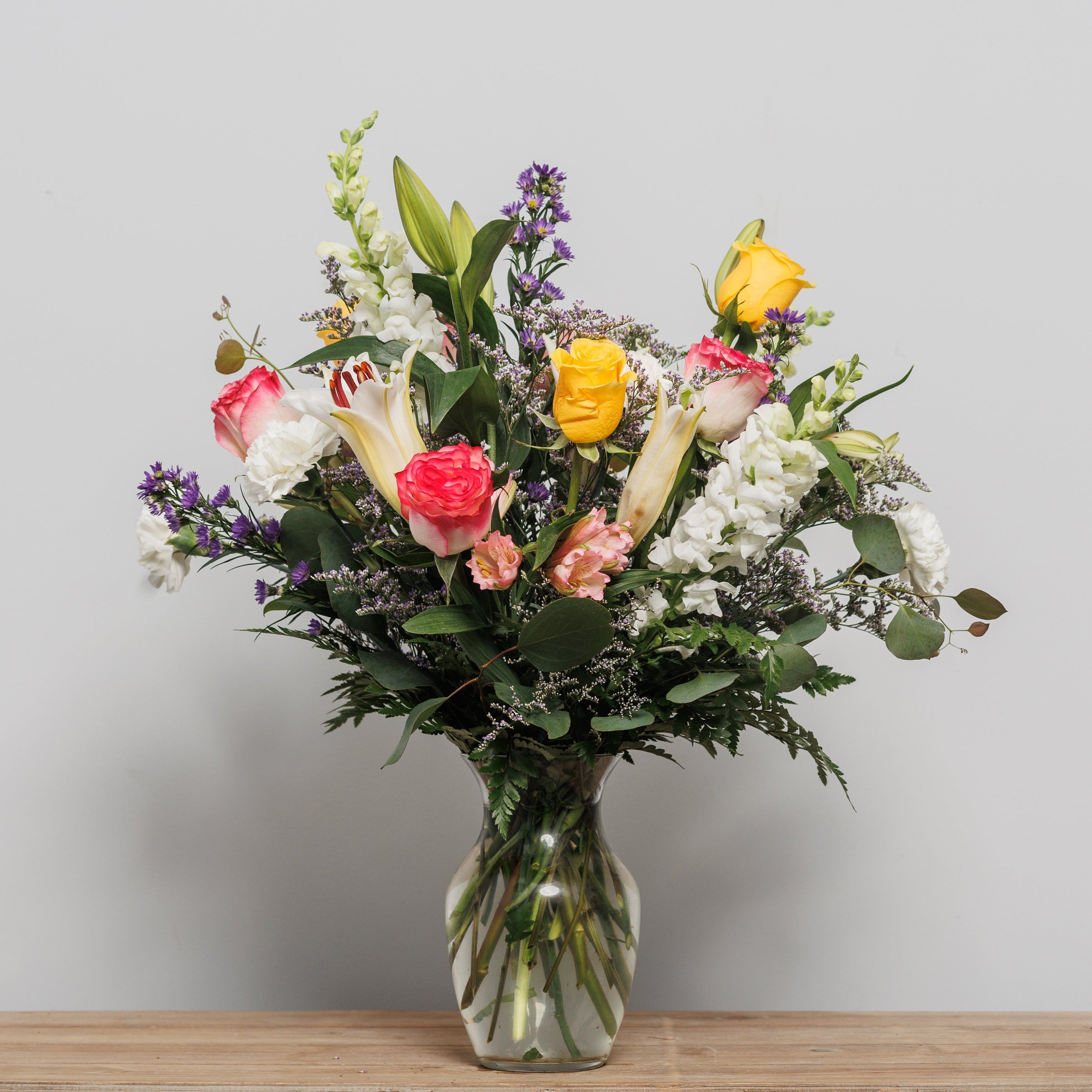 A colorful mix of roses, lilies and snap dragons arranged in a vase.