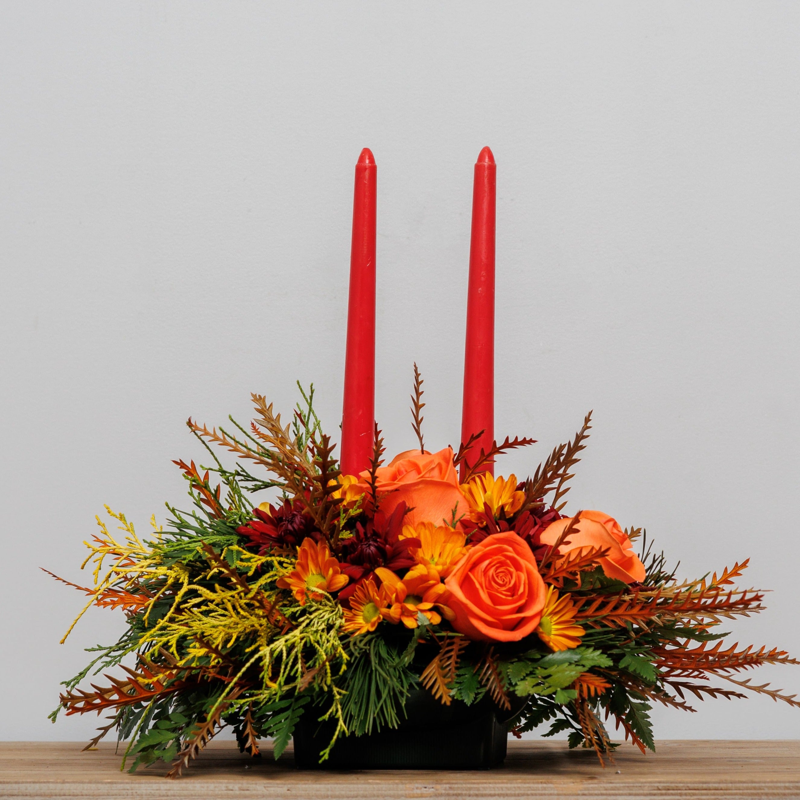 A fall centerpiece with orange roses, fall foliage and 2 red taper candles.