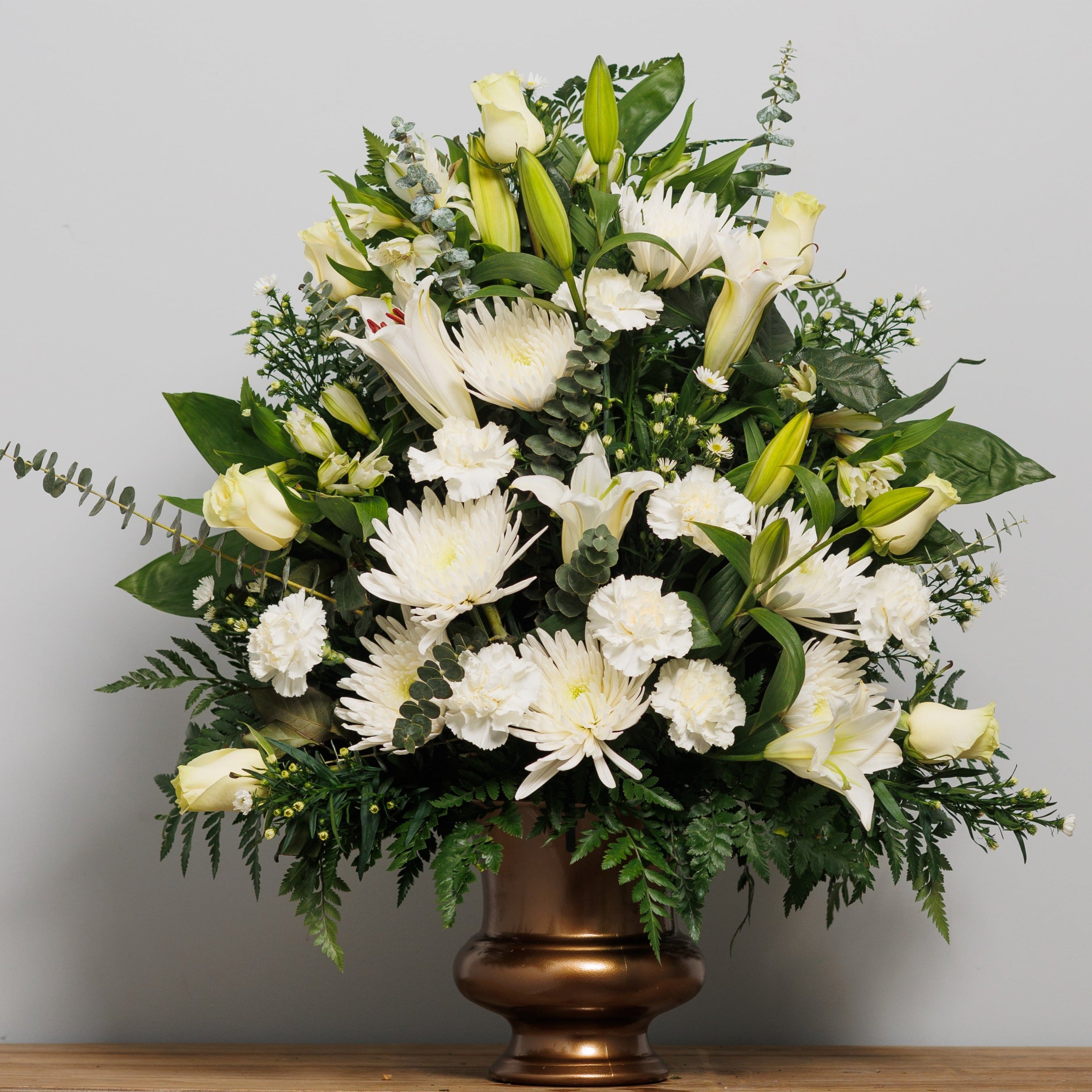 An all white floral arrangement in a bronze urn.