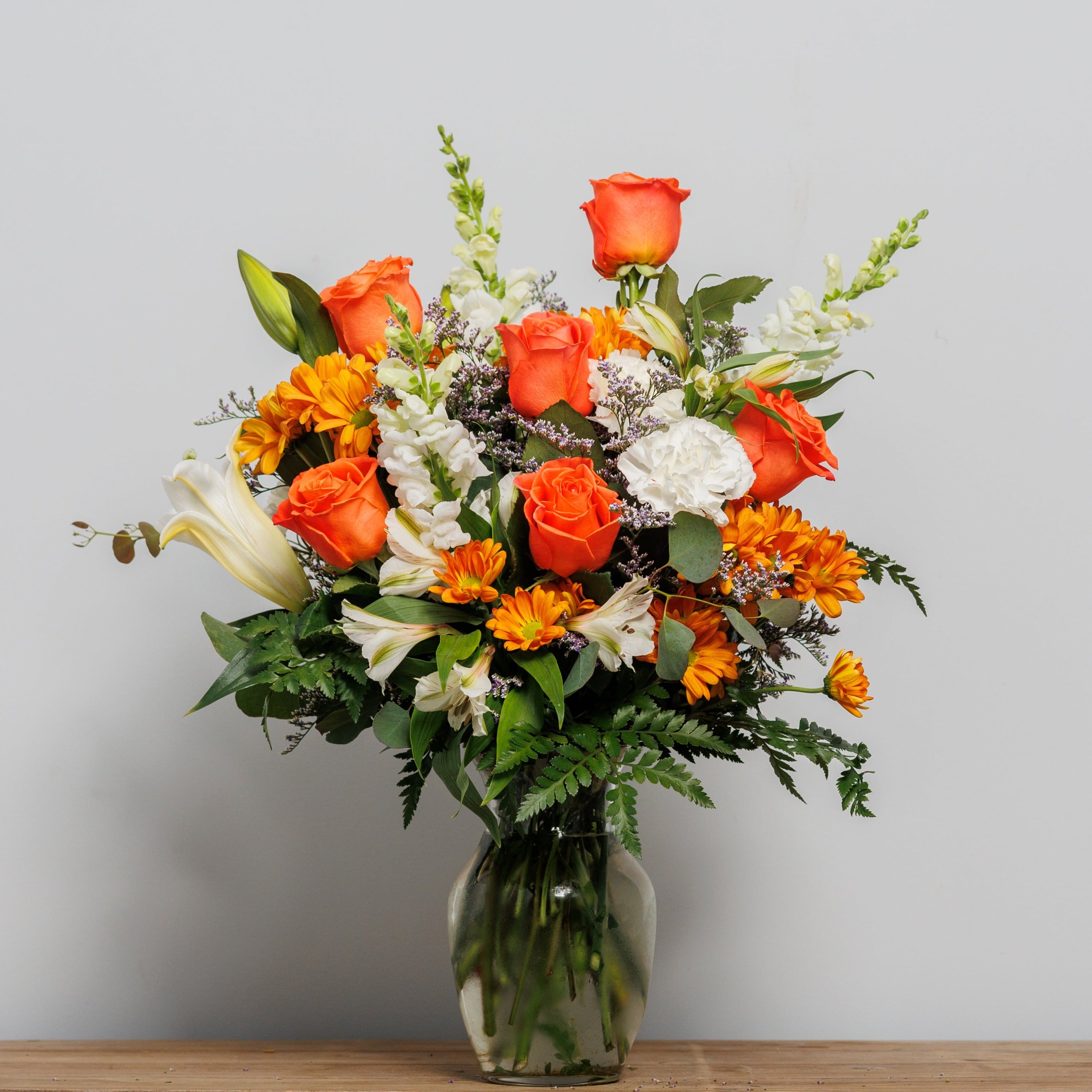 A vase arrangement with white lilies and white snap dragons and orange roses.