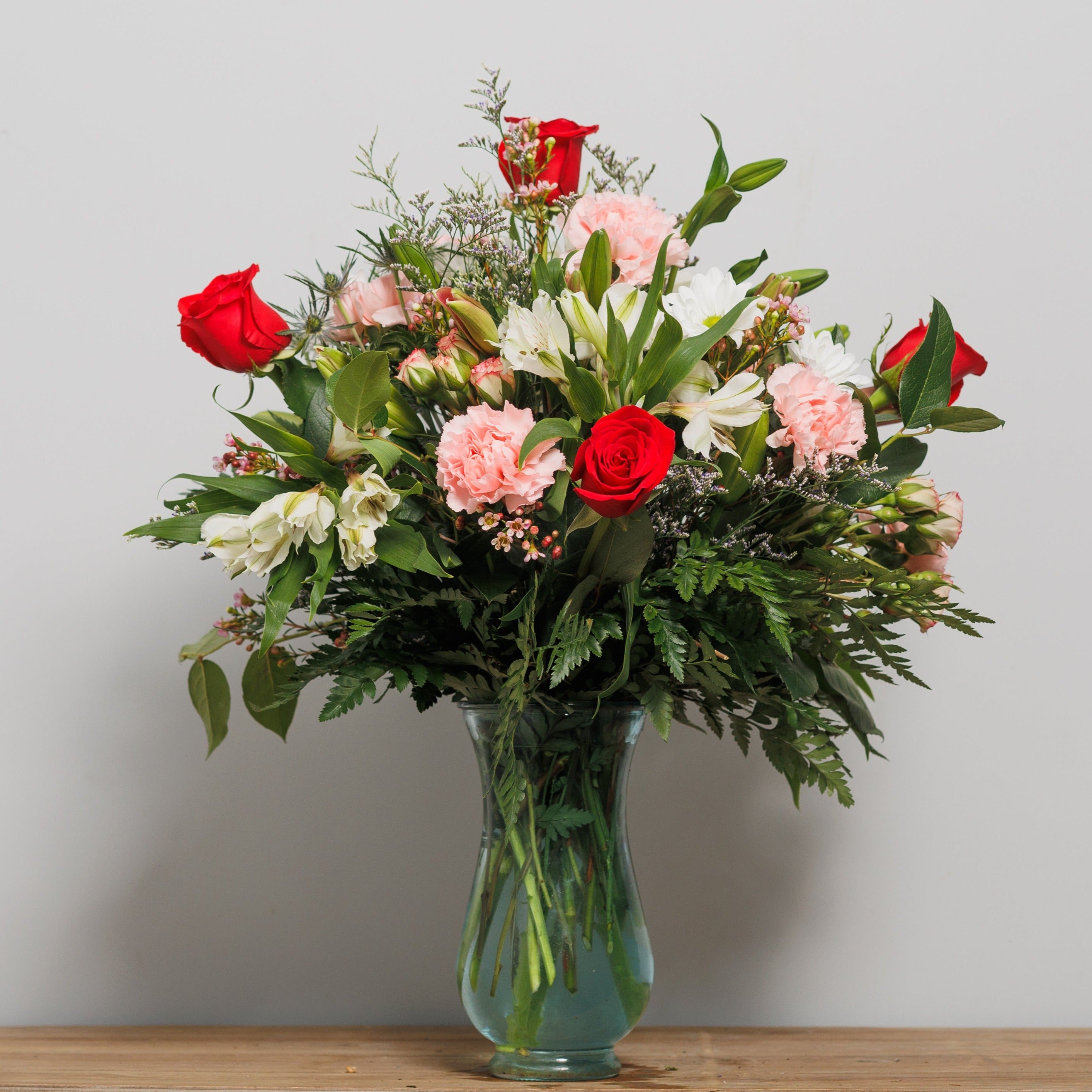 Red roses with pink carnations, lilies and alstroemeria arranged in a vase. 