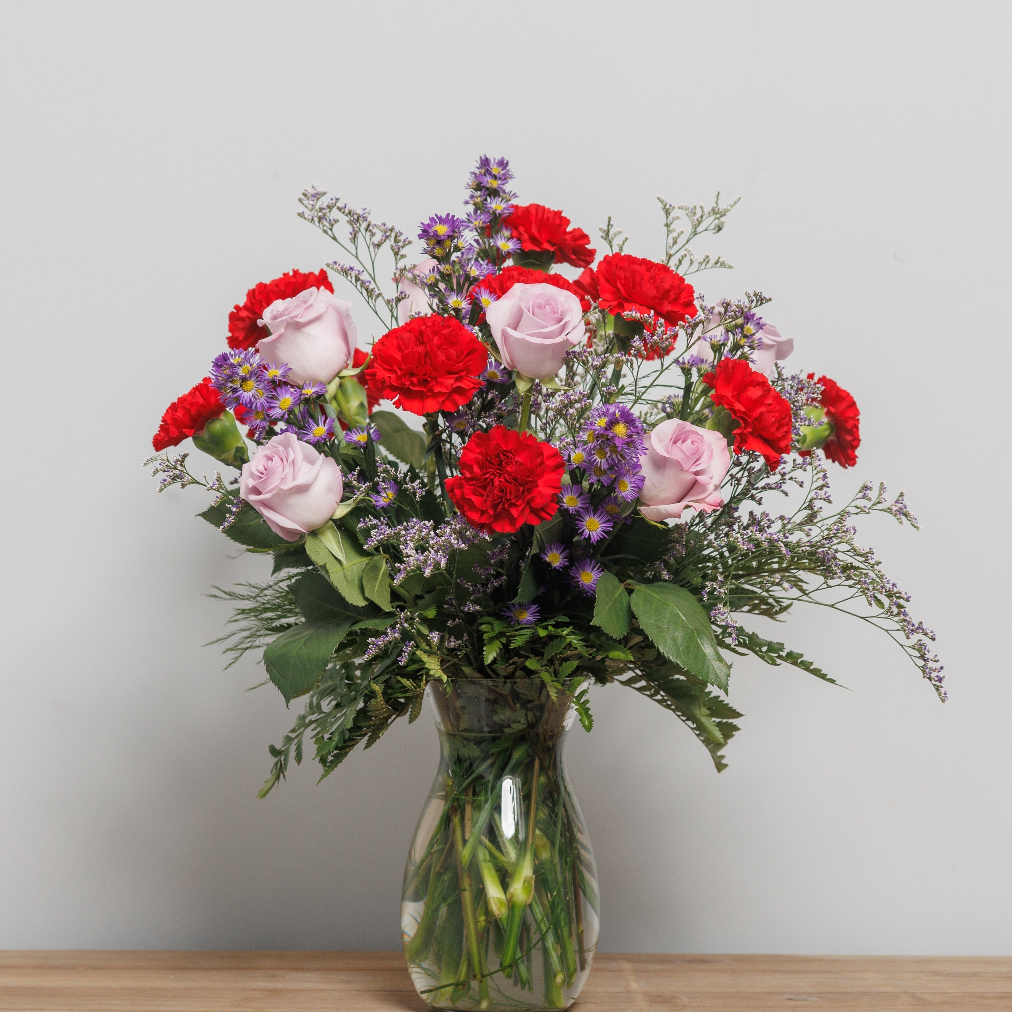 A vase arrangement with red carnations and lavender roses.