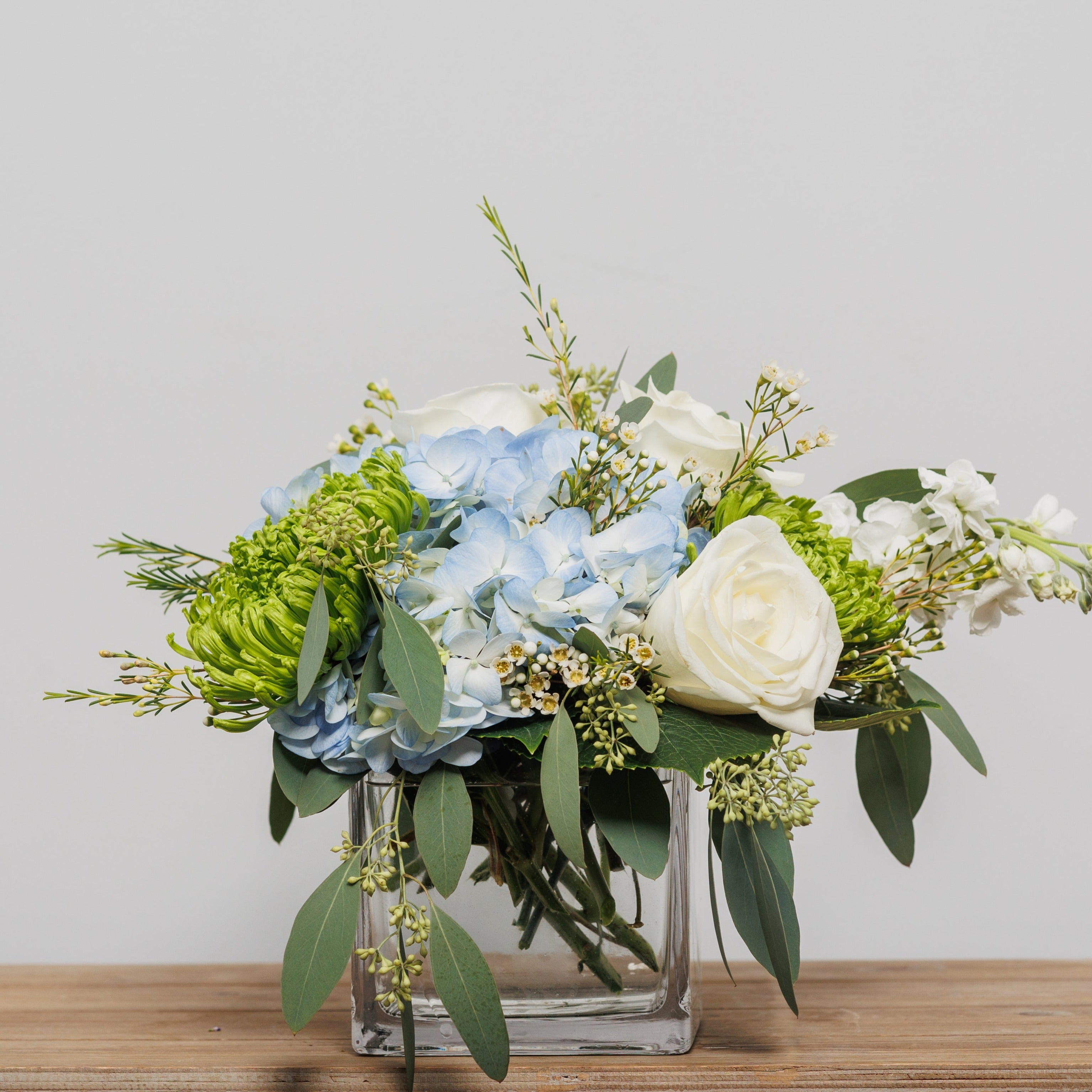 A cube arrangement with blue hydrangea, green spider mums and white roses.