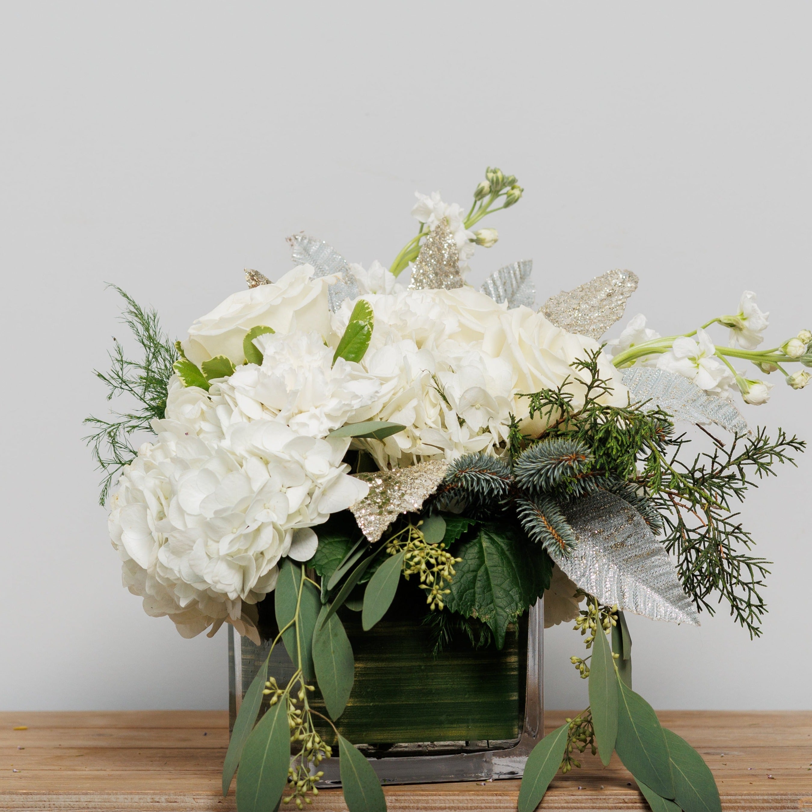A cube arrangement with white hydrangeas, white roses and glitter stems.