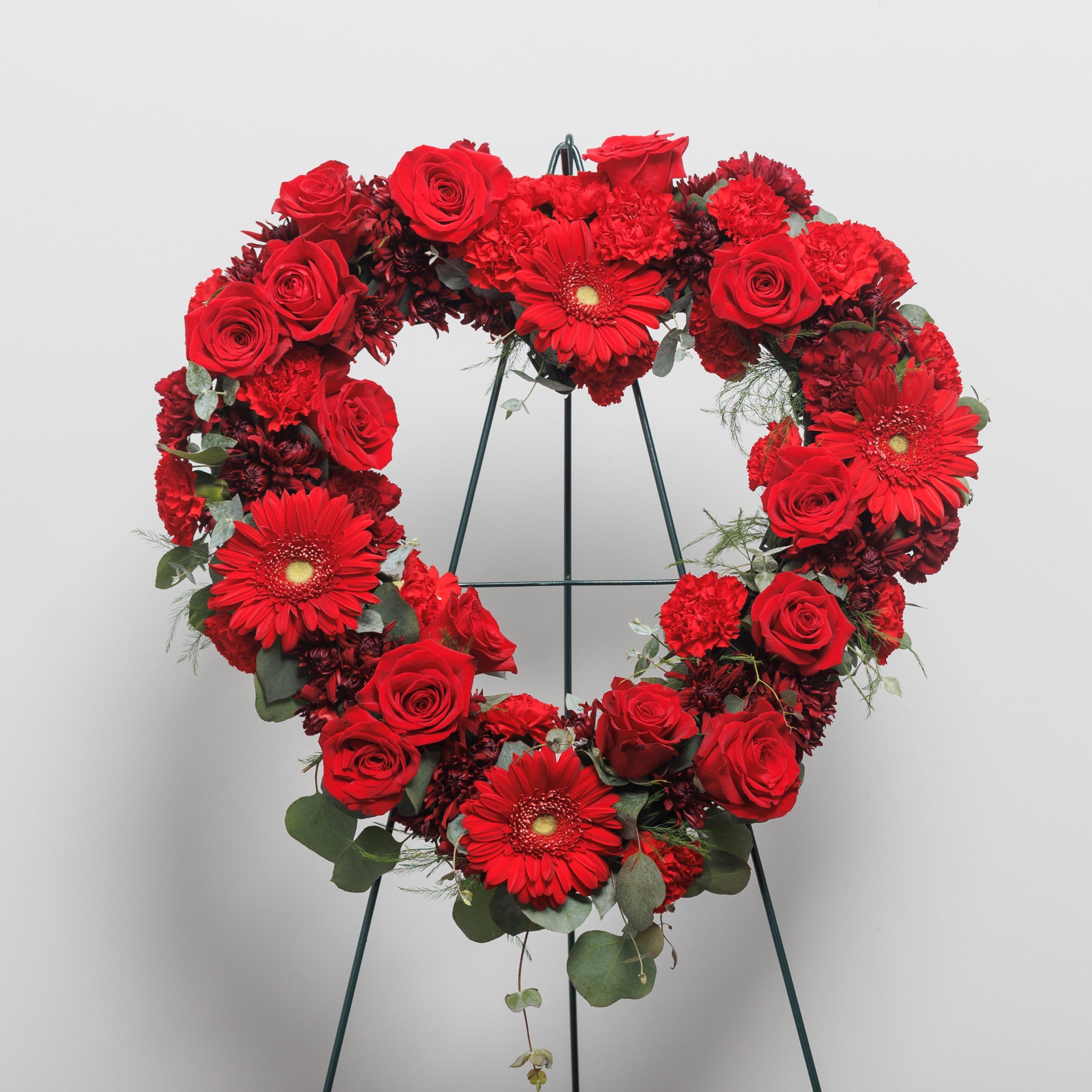 A heart wreath spray with red roses, red gerber daisies and red carnations.