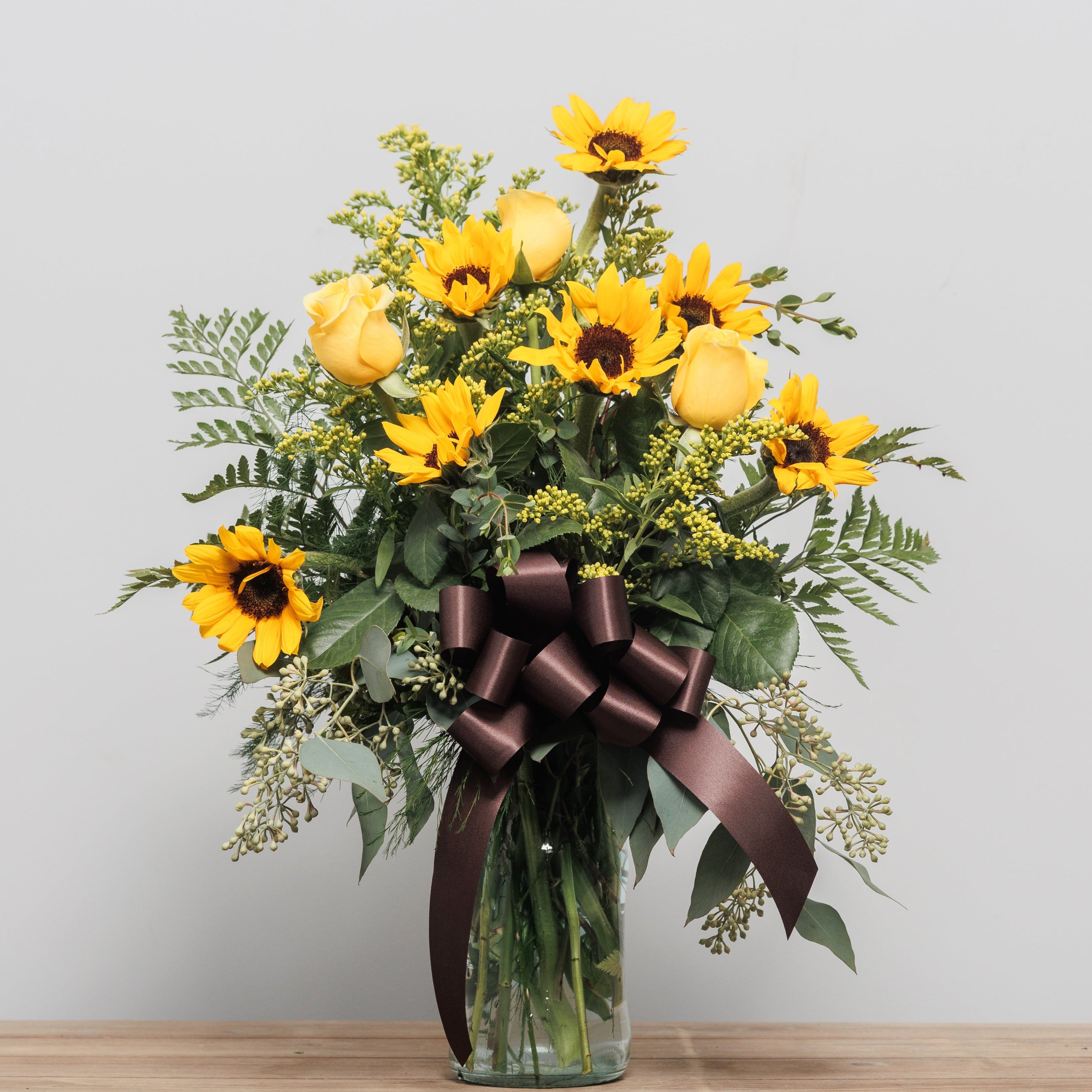 Yellow roses and sunflowers in a vase with a chocolate bow