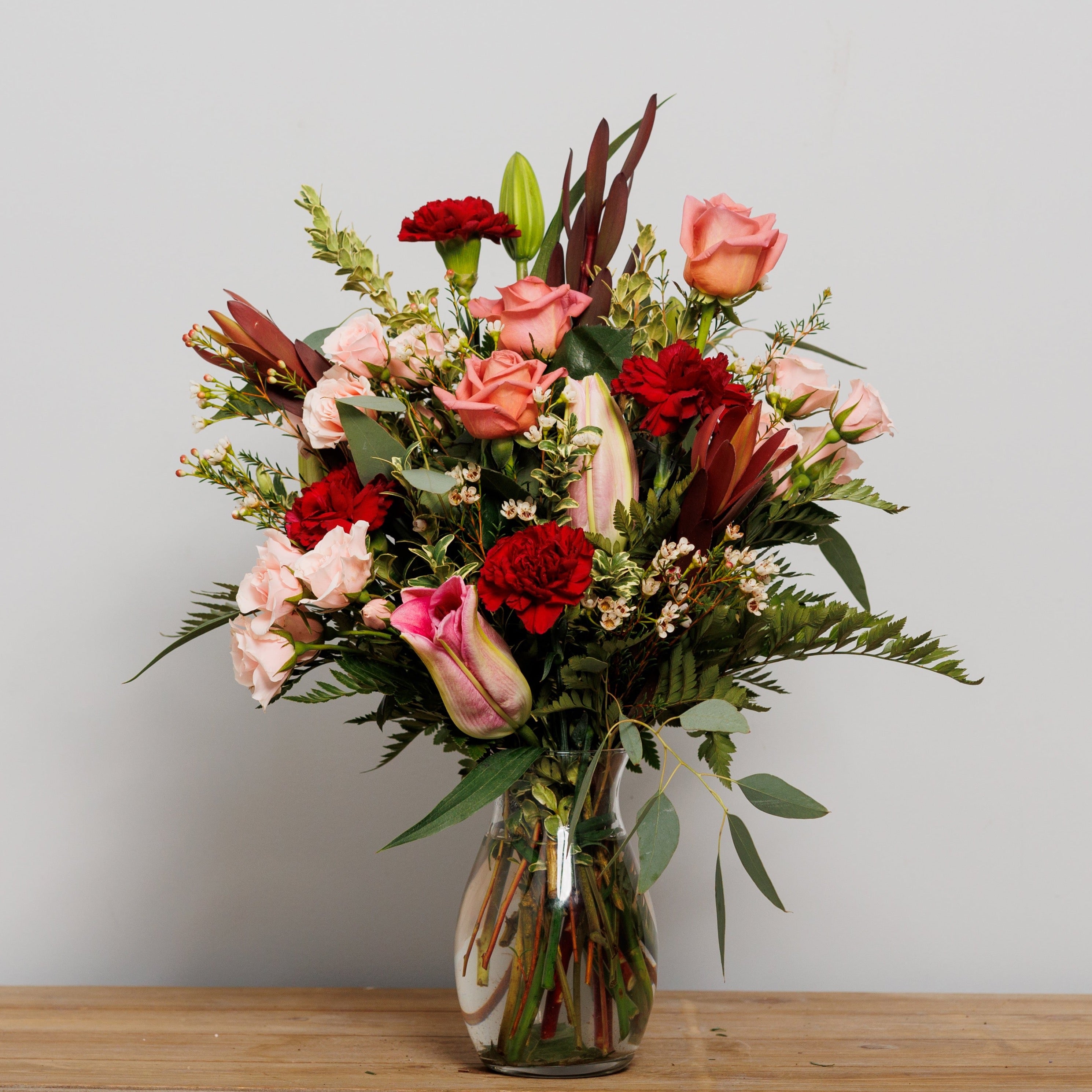 A vase arrangement with dark red carnations and lilies and pink roses.