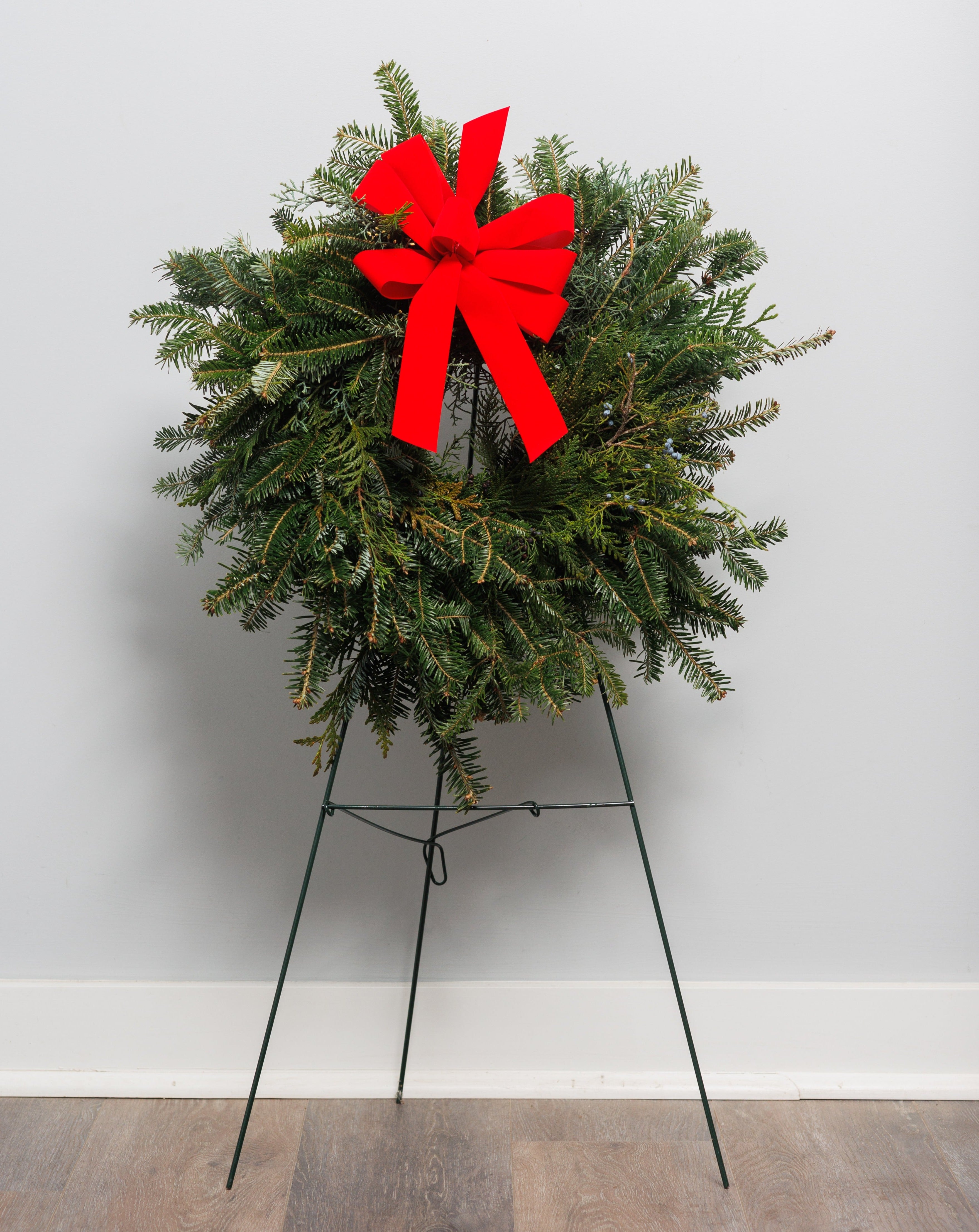 A fraser fir wreath on an easel with a red velvet bow.