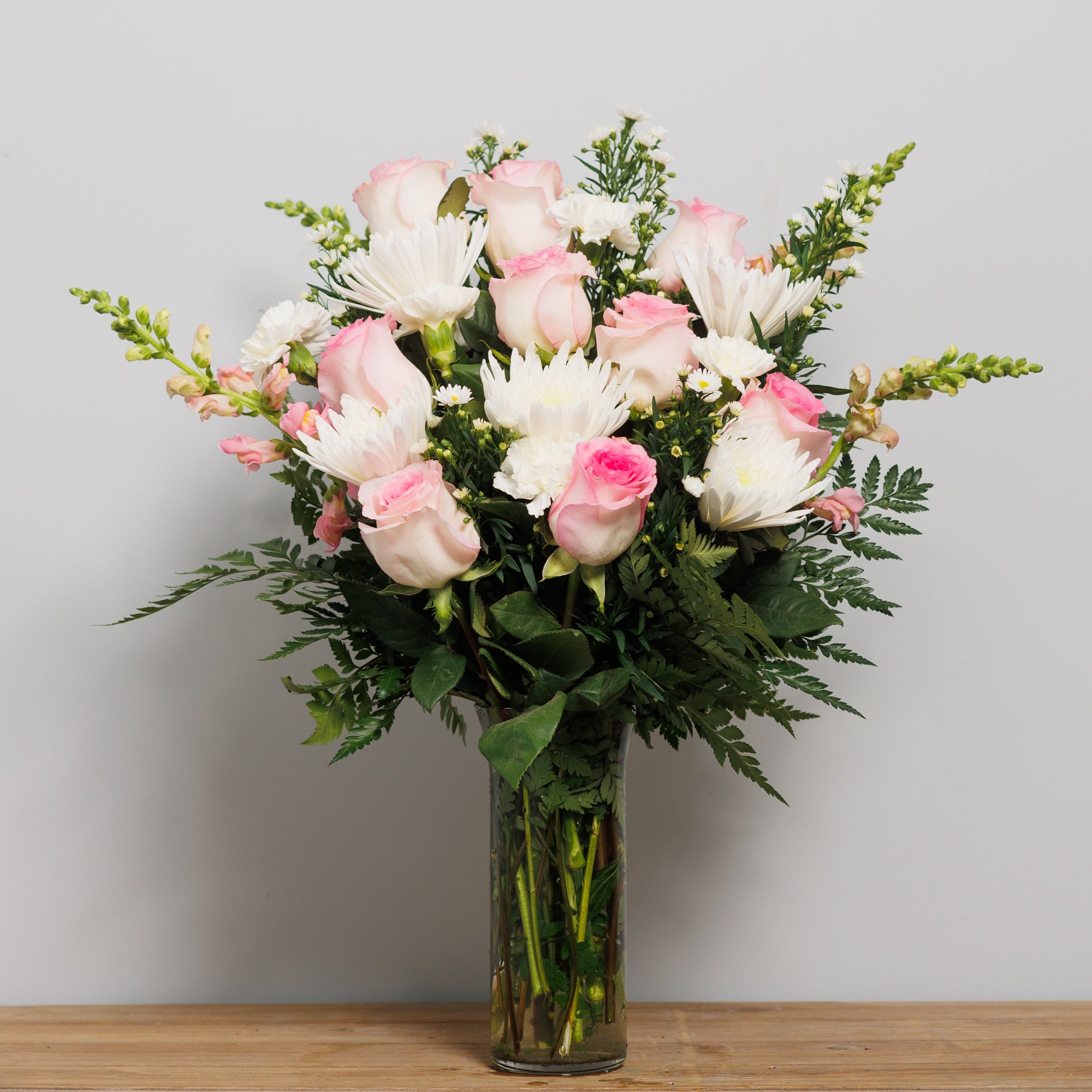 A vase arrangement with light pink roses and white mums.