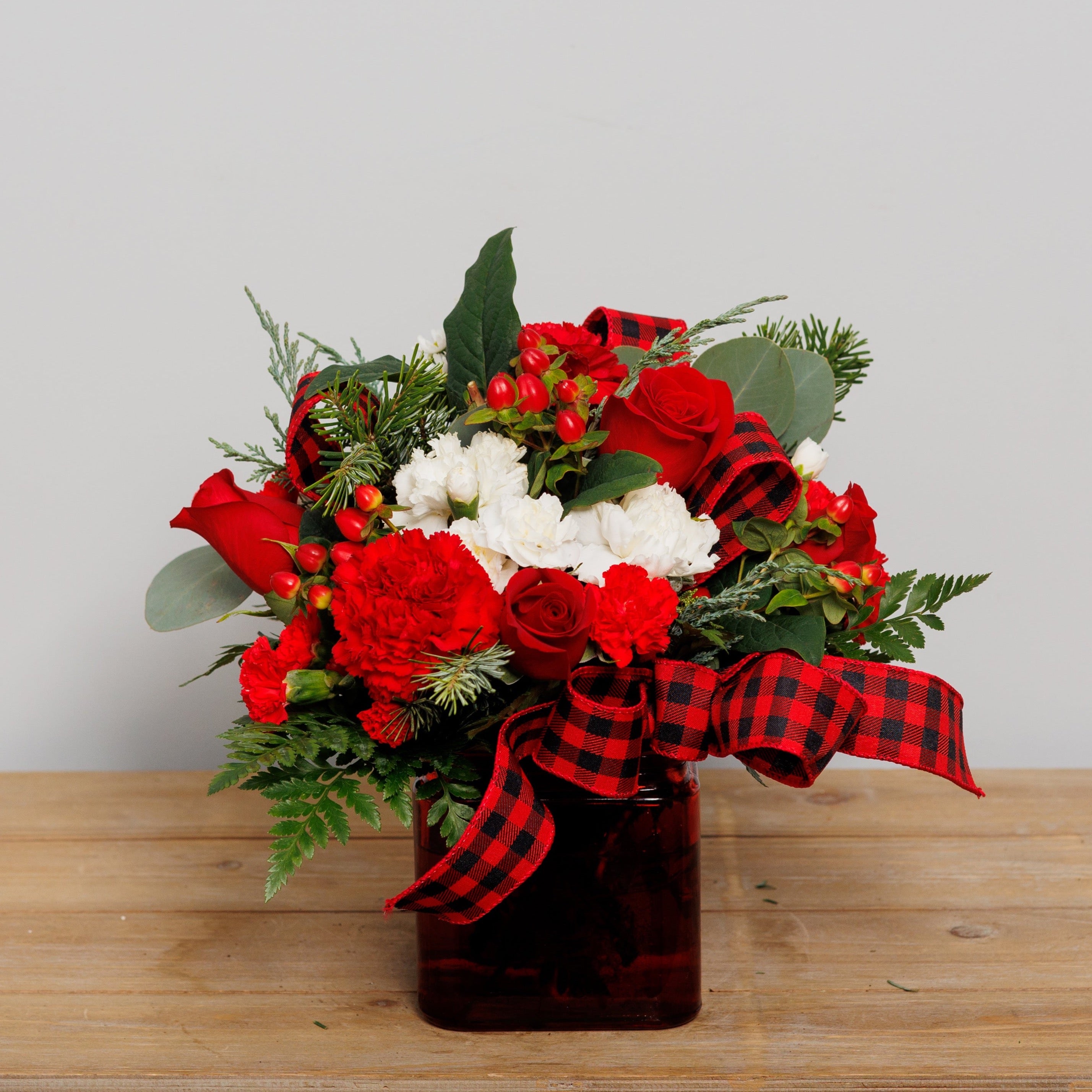 A red and white arrangement in a red cube with buffalo plaid ribbon.