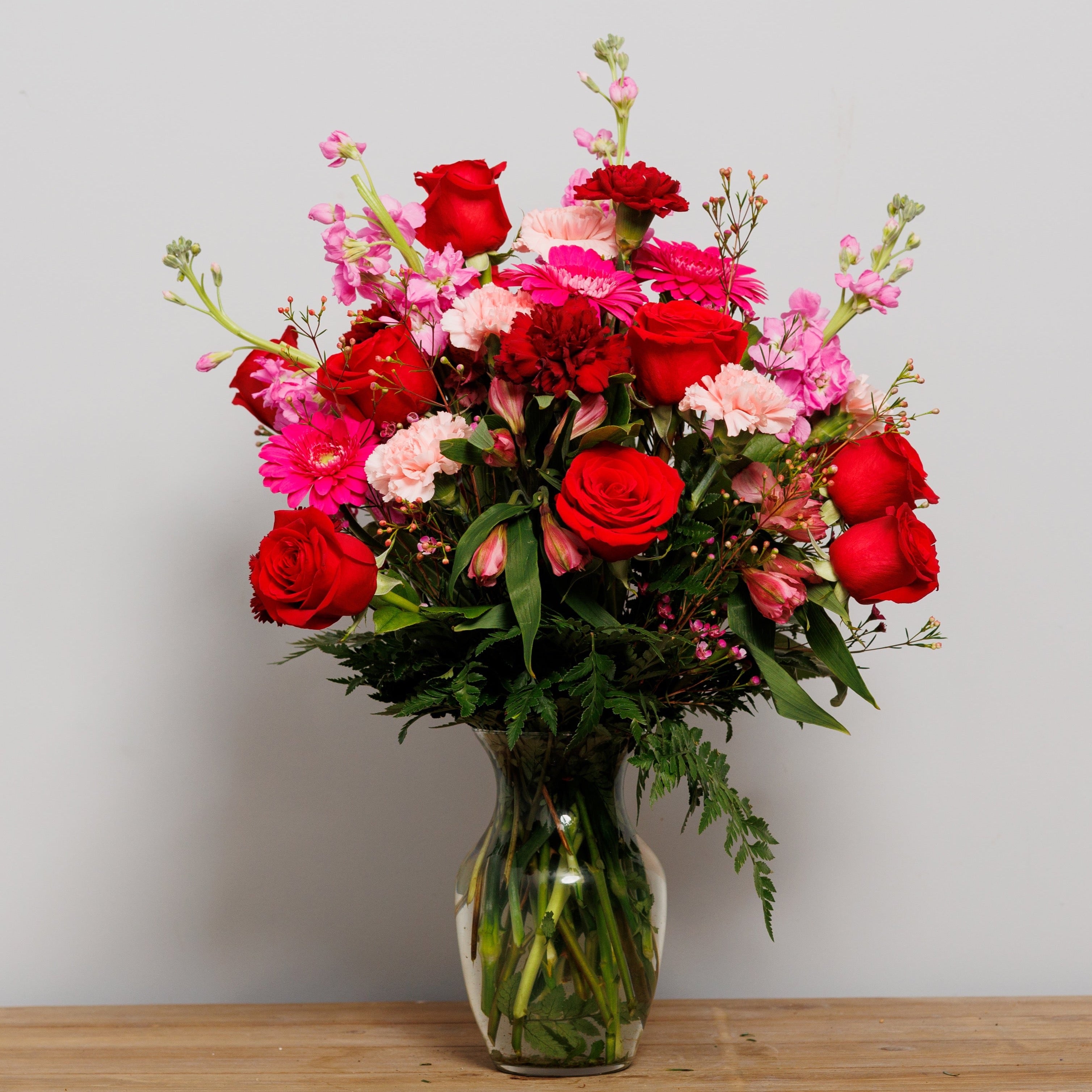 A vase arrangement with hot pink Gerber daisies, red roses and pink carnations.