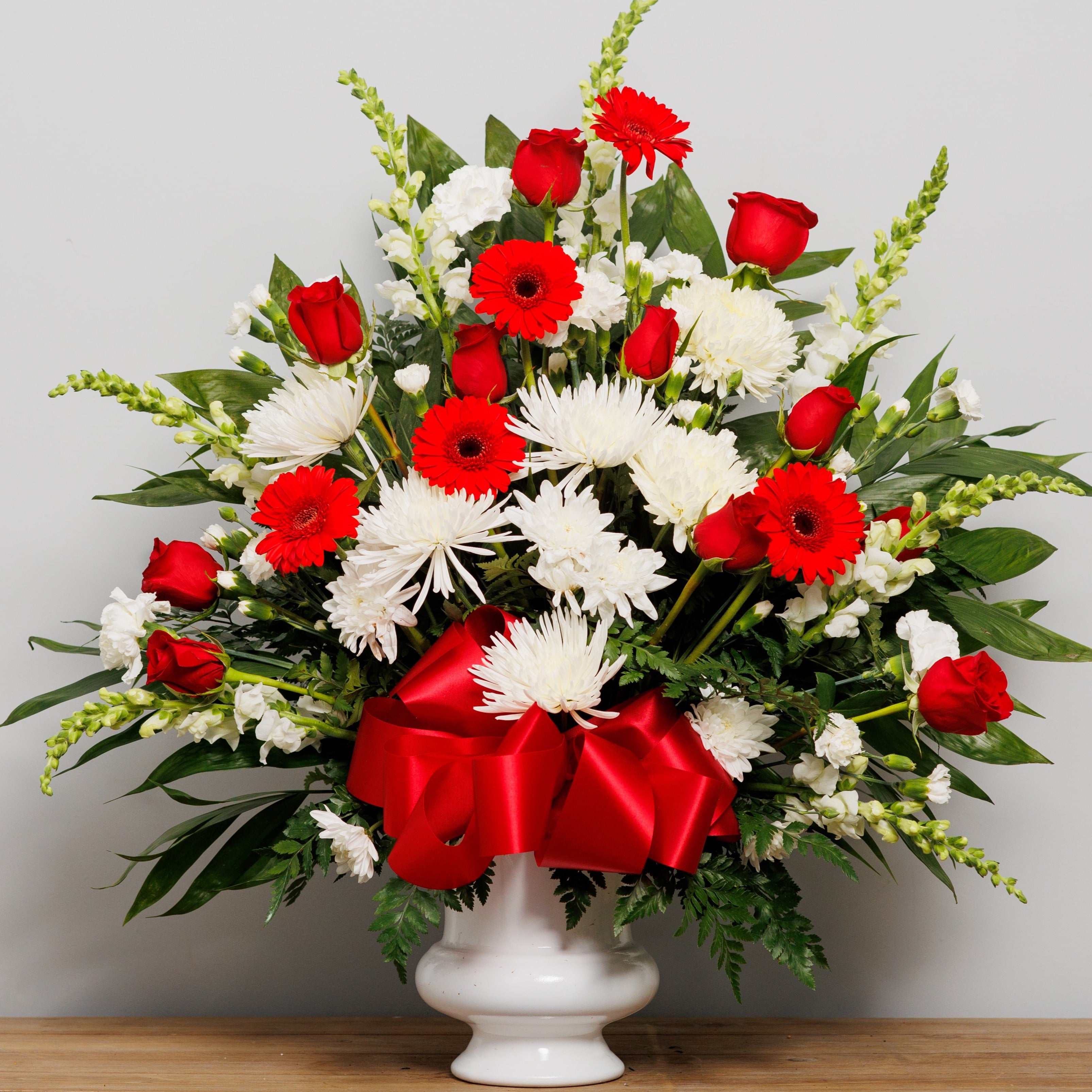 An urn arrangement with all red and white flowers.