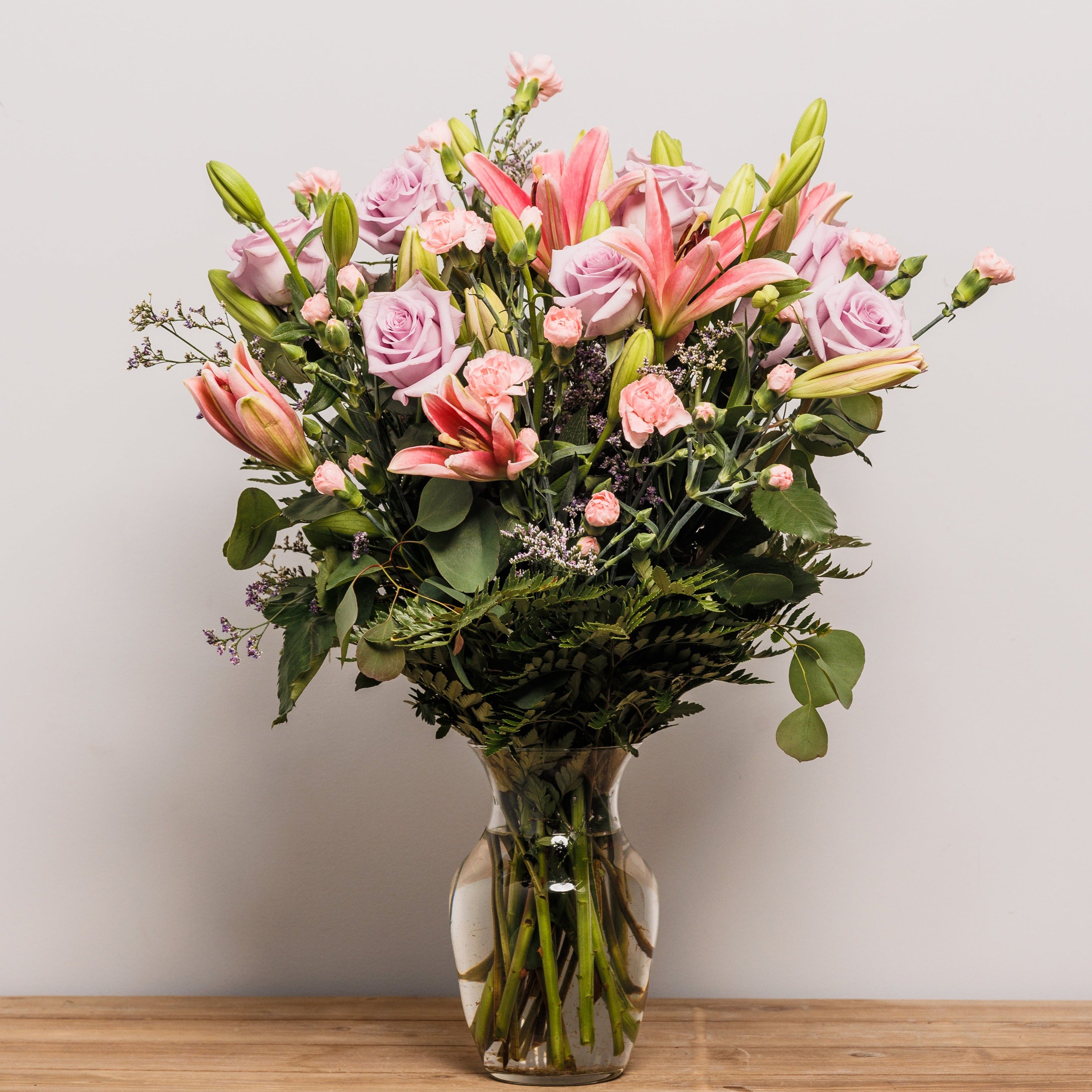 Light pink lilies with lavender roses in a vase.