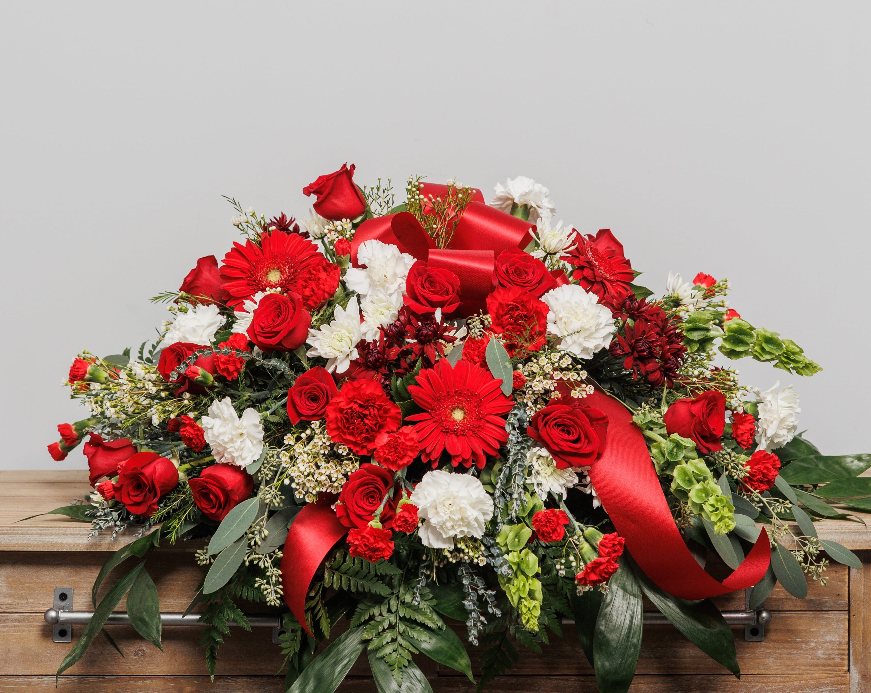 A casket spray with red gerber daisies, red roses and white carnations.