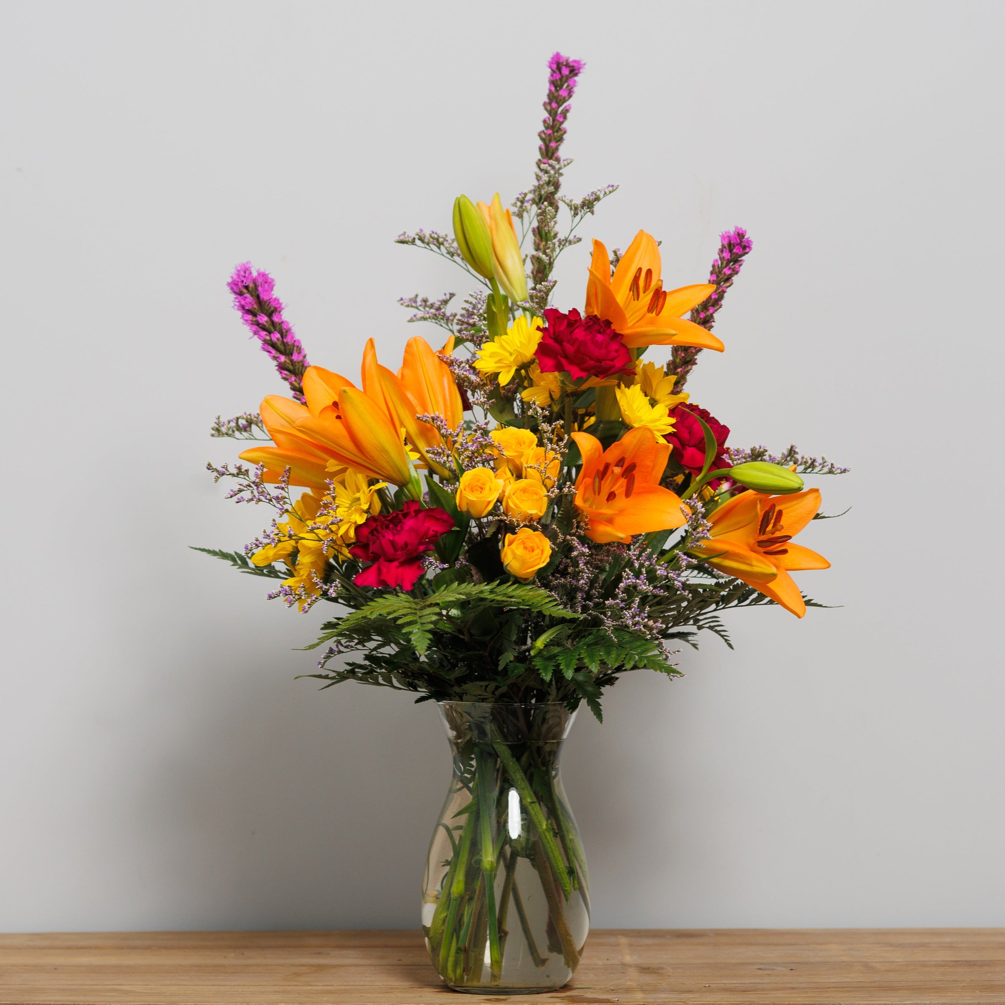 A floral arrangement with orange lilies, yellow spray roses and fuchsia liatris.  