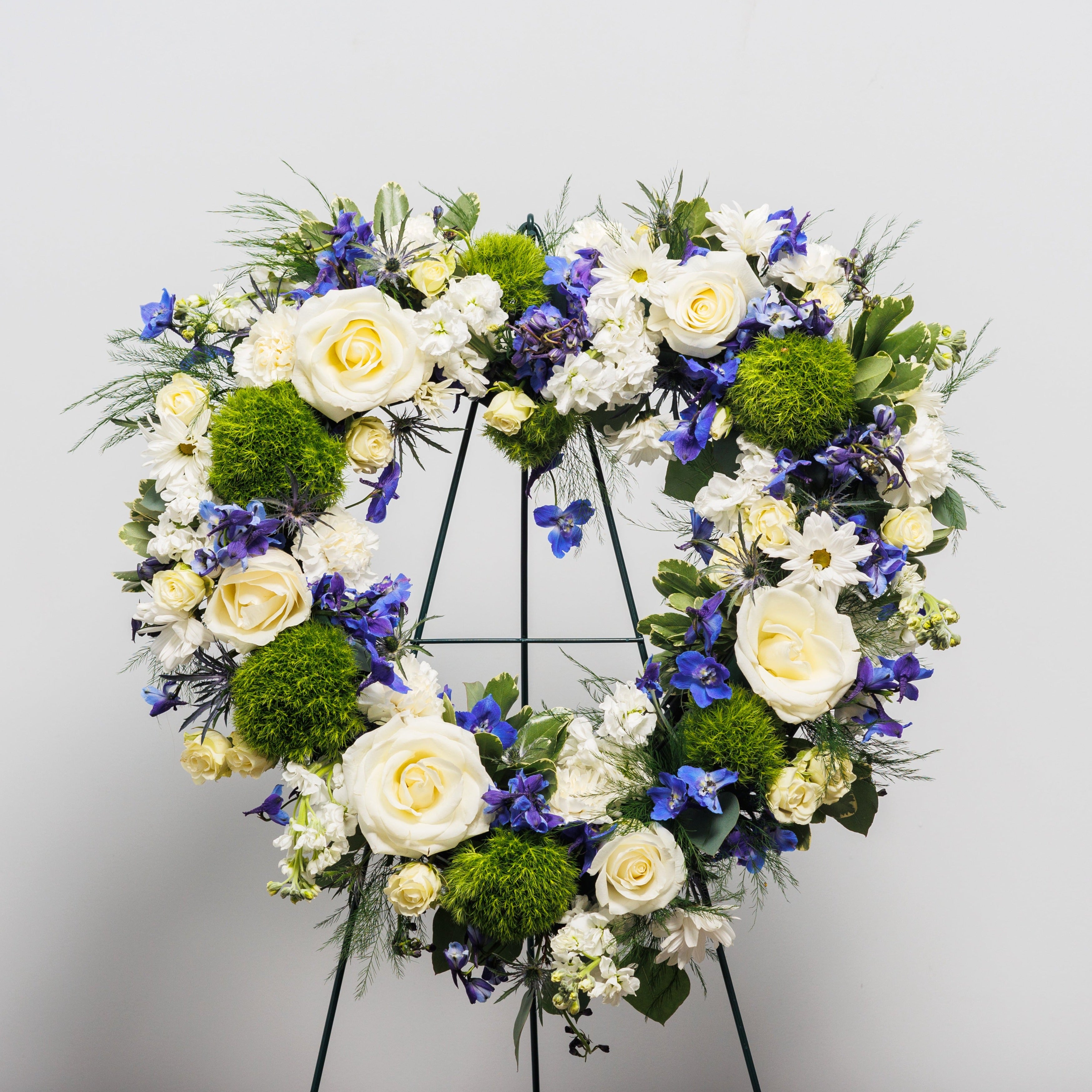 An open heart standing spray with white, green and blue flowers.