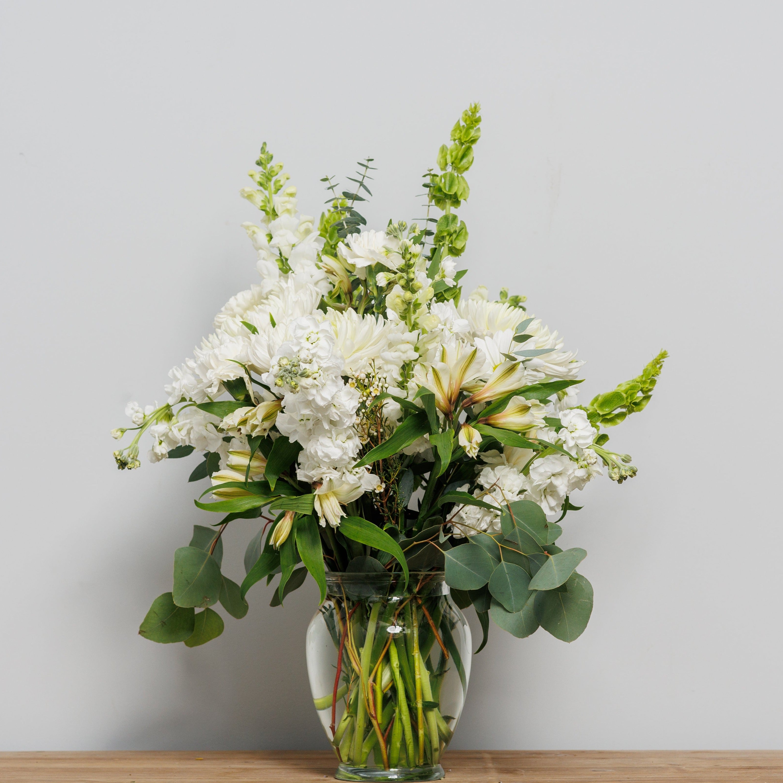 A white and green arrangement with mums and bells of Ireland.